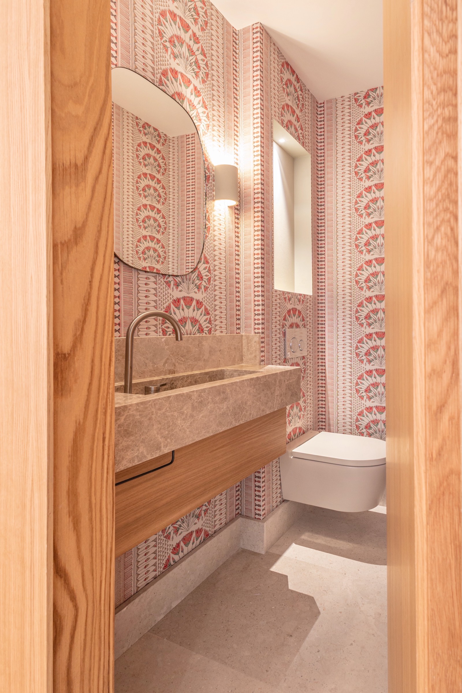 Cuarto de baño moderno con papel tapiz de patrón rosado, lavabo de piedra gris, mueble de madera y inodoro blanco suspendido