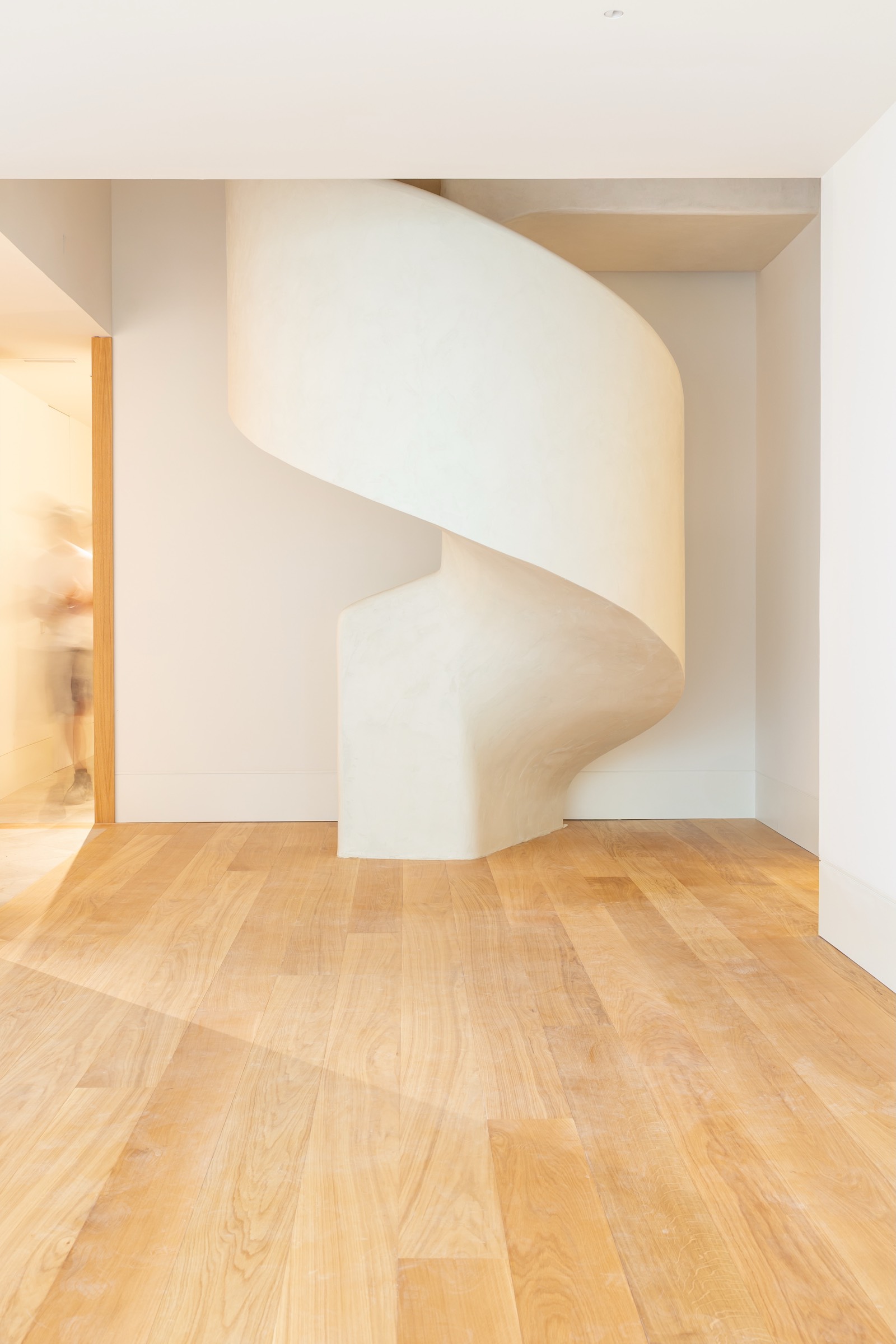 Escalera blanca curva y fluida con diseño minimalista, instalada en un espacio interior con piso de madera clara