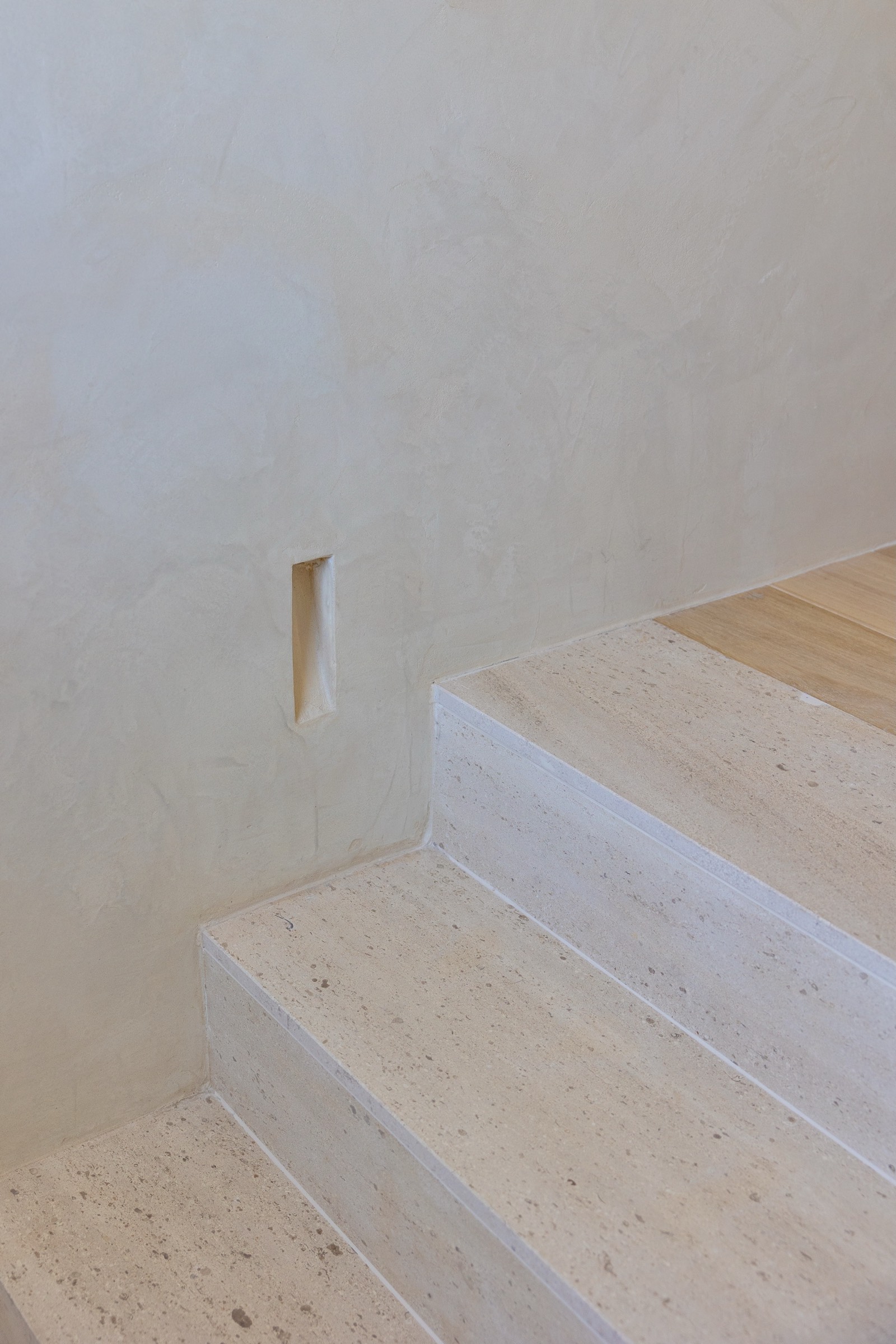 Escaleras de concreto neutras con textura granulada, en un espacio arquitectónico minimalista con pared beige y detalle de nicho pequeño