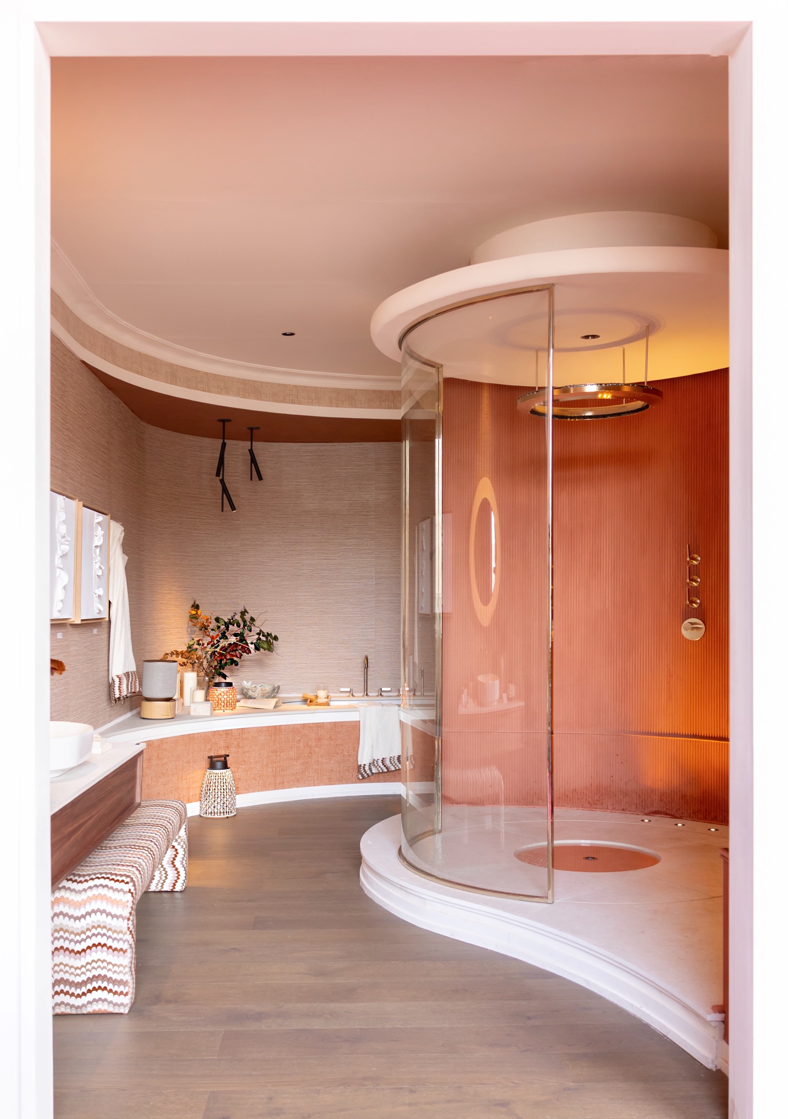 Baño elegante con ducha circular de vidrio transparente, paredes en tonos rosados y naranjas, y detalles decorativos sutiles