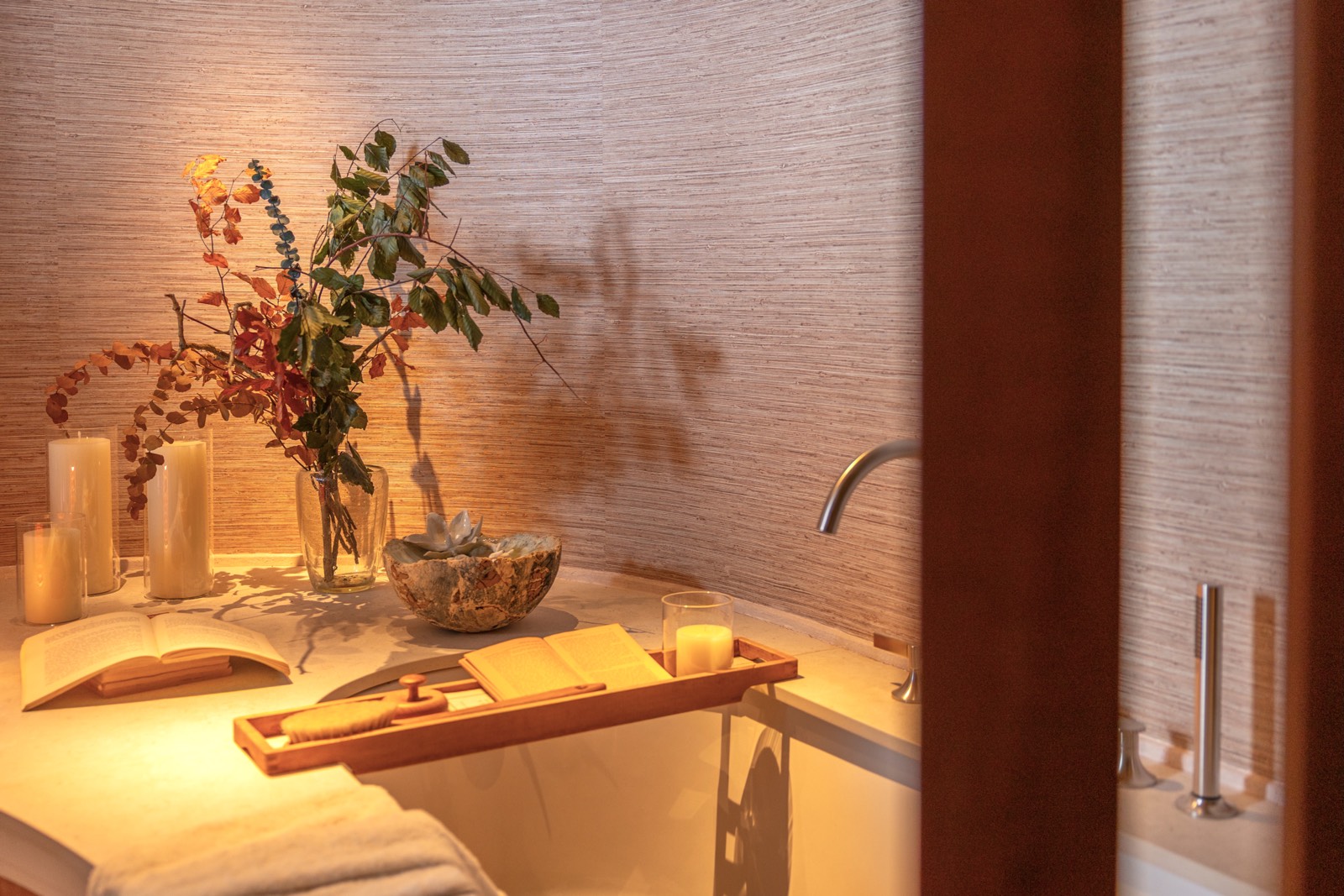 Ambiente de spa con velas, flores secas, libro abierto y toallas blancas bajo una iluminación cálida y acogedora