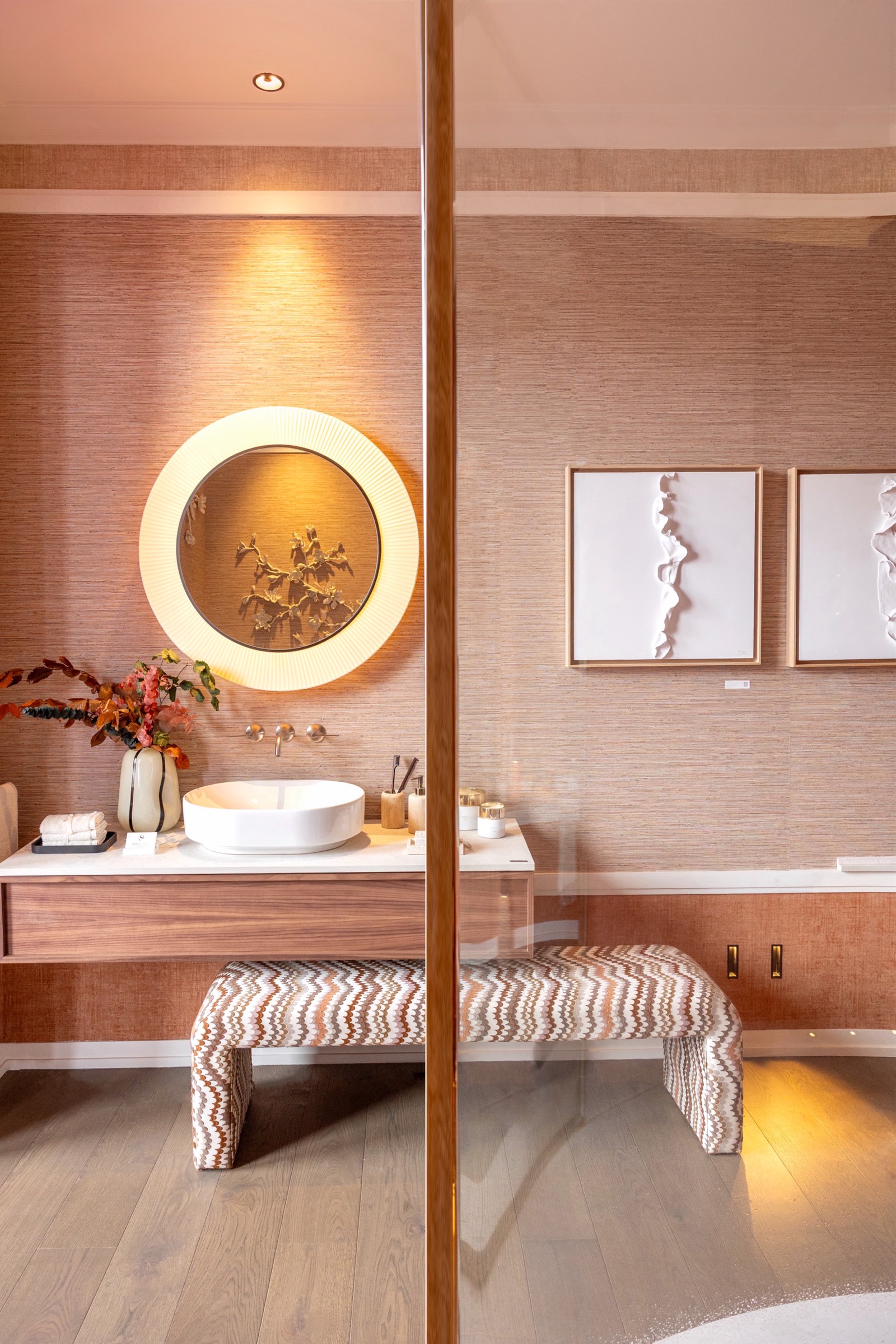 Diseño interior de un baño moderno con lavabo redondo blanco, espejo circular iluminado y bancos decorativos con patrón zigzag