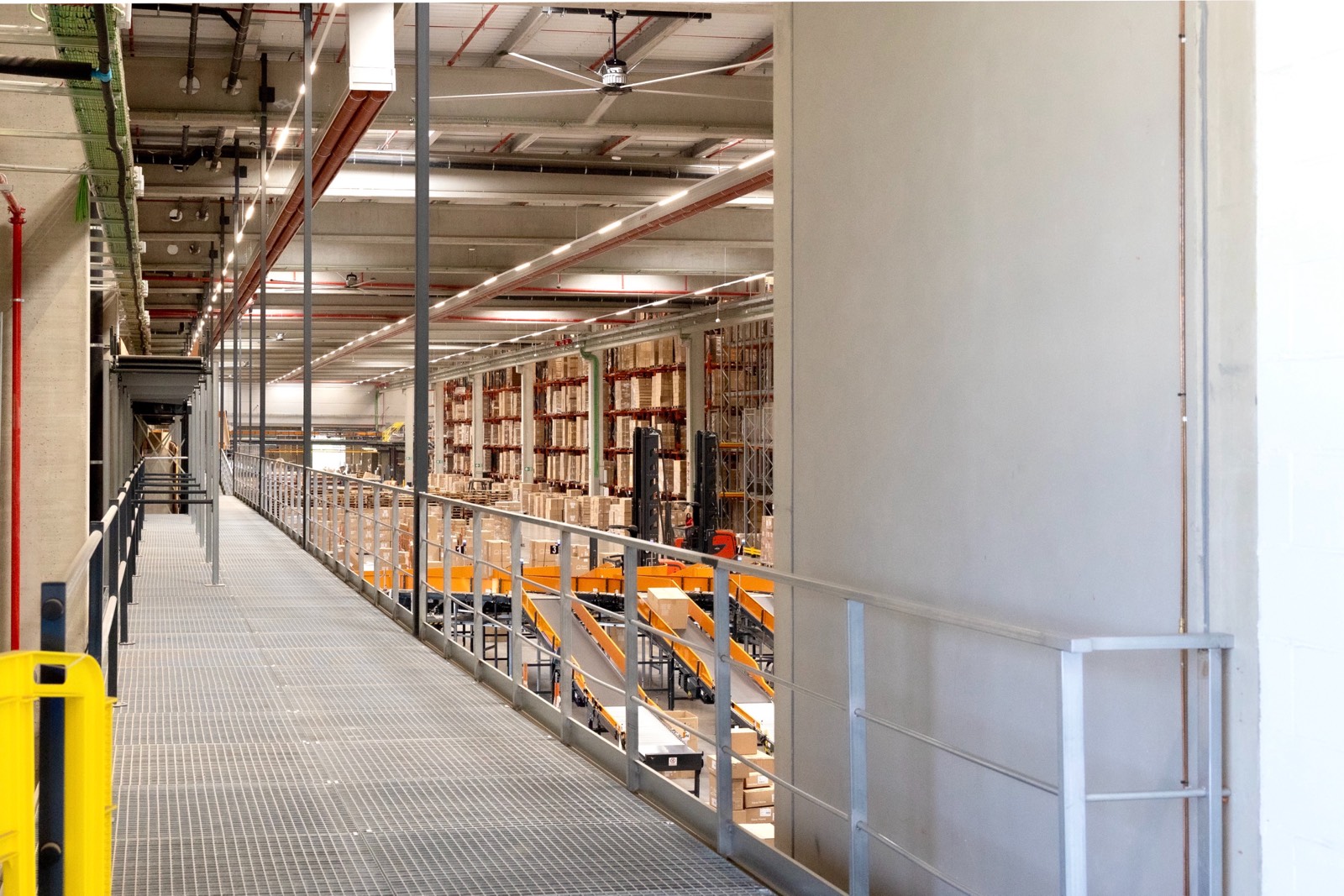 Vista interior de un almacén industrial moderno con pasarela metálica, estanterías de carga y sistemas de almacenamiento de altura