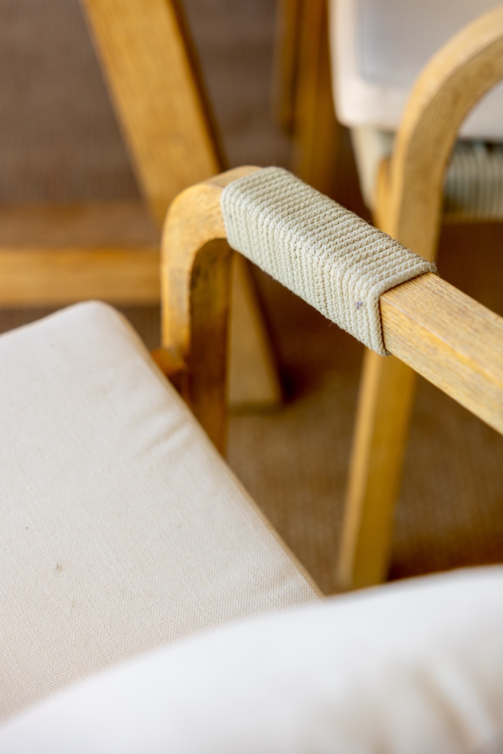 Primer plano de una silla de madera con un detalle de cuerda enrollada alrededor del reposabrazos. El asiento está cubierto con una tela blanca.