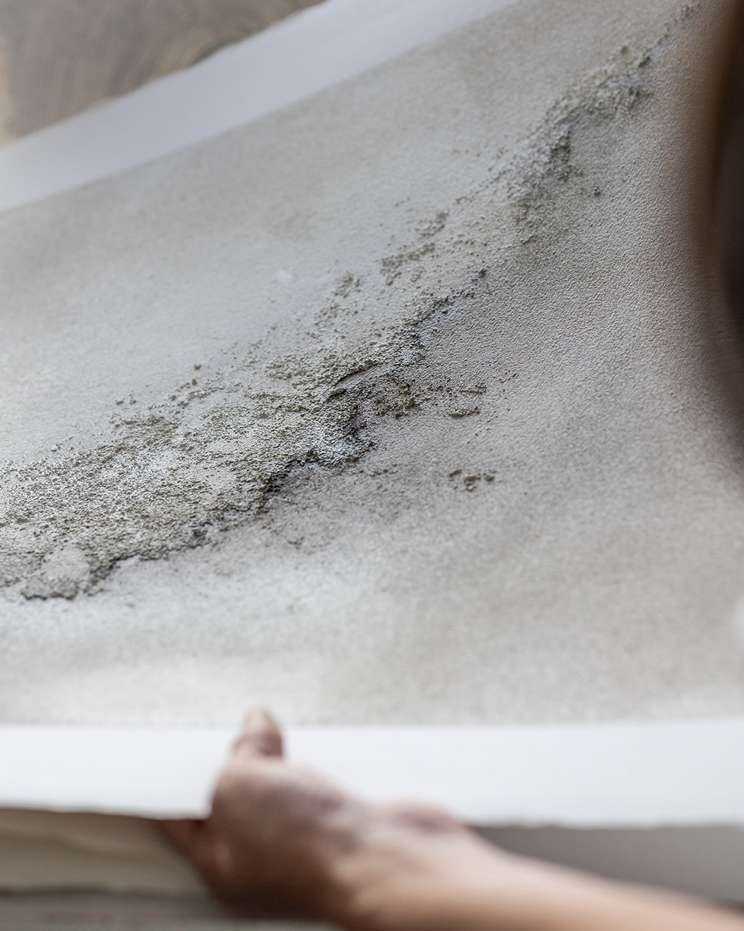 Primer plano de una pared blanca con manchas de moho negro. Una mano sostiene el borde inferior de la imagen, mostrando la escala del problema de humedad.