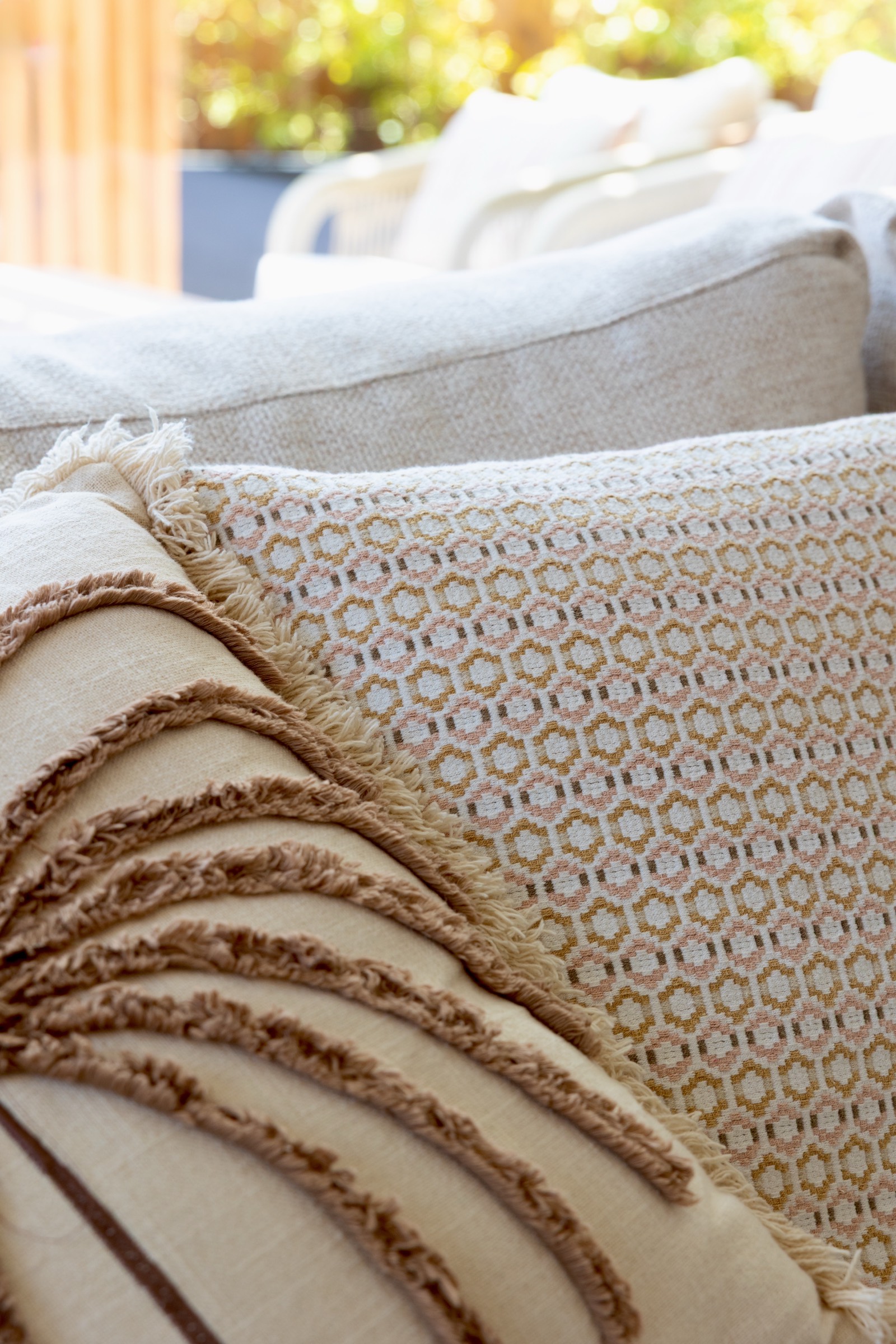 Primer plano de cojines decorativos en tonos neutros sobre un sofá. Un cojín tiene un patrón geométrico en beige y otro tiene flecos marrones. La imagen transmite una sensación de confort y estilo en decoración de interiores.