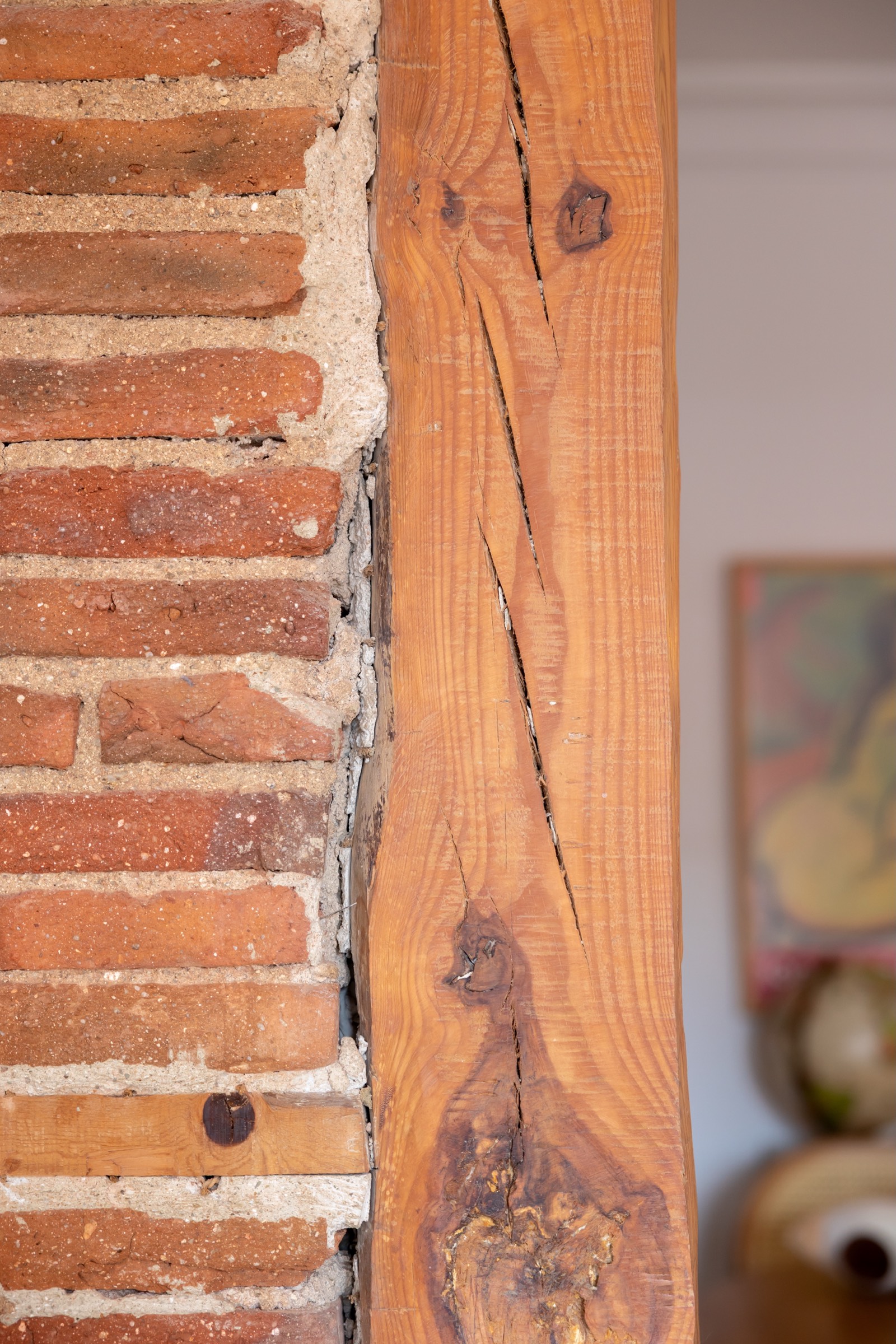 Detalle de una pared con ladrillo rojo terracota y una viga de madera desgastada con grietas y nudos