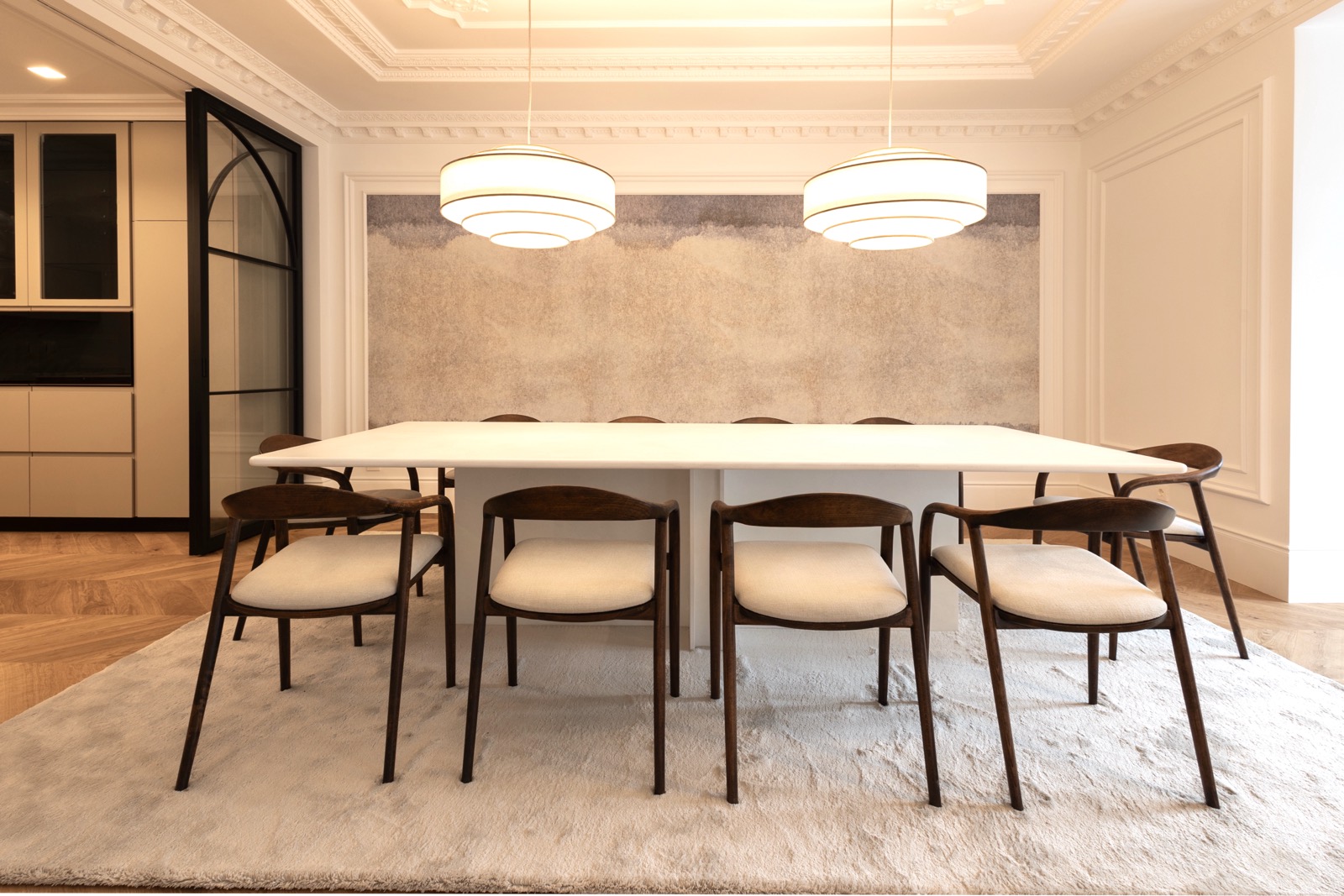 Comedor elegante con mesa blanca rectangular, sillas de madera oscura con asientos claros, lámparas colgantes redondas y decoración minimalista en tonos neutros.