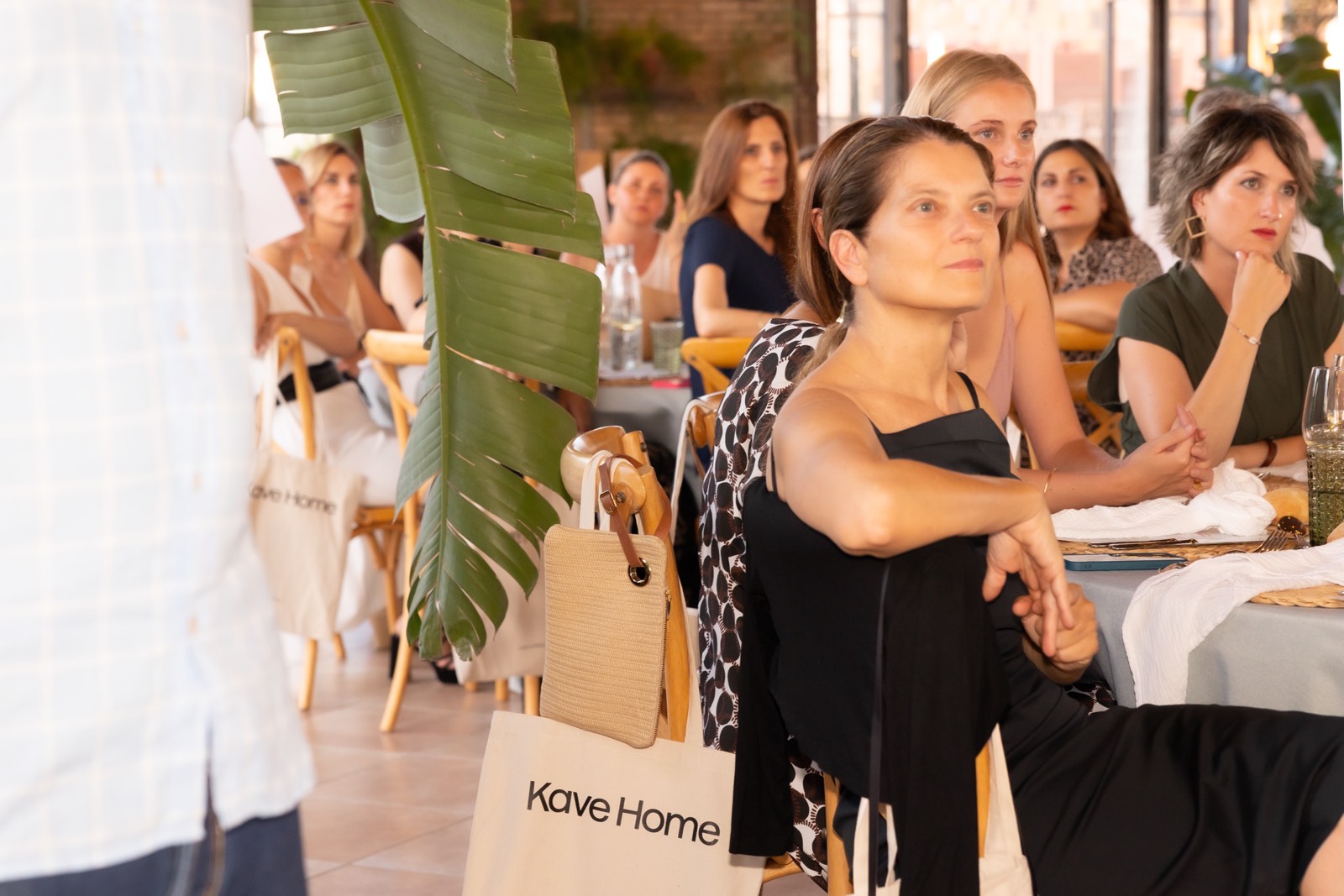 Grupo de mujeres sentadas en un evento de Kave Home, con bolsas de marca y decoración con hojas verdes