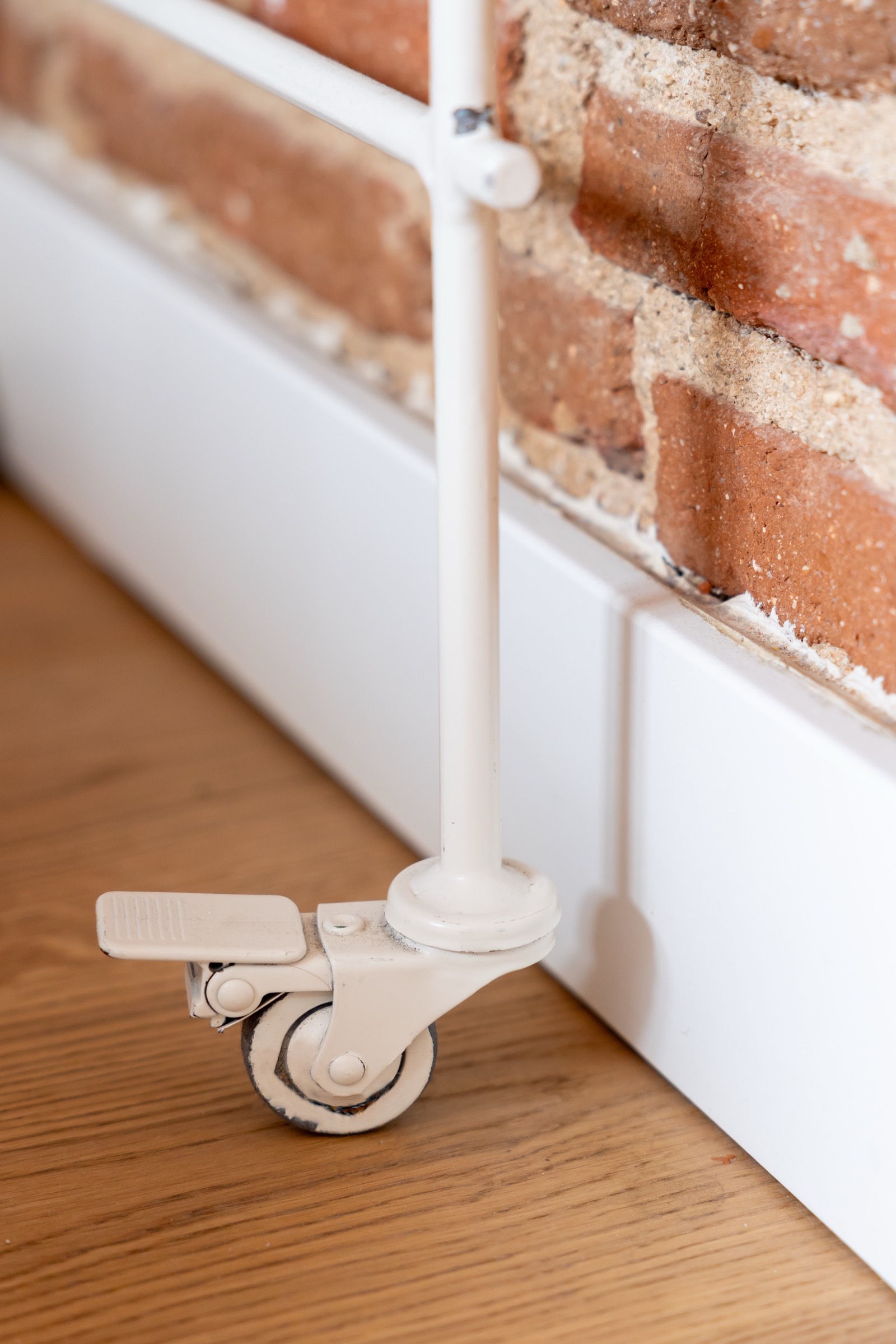 Rueda blanca giratoria de mueble montada en base blanca, junto a pared de ladrillo rojo y piso de madera