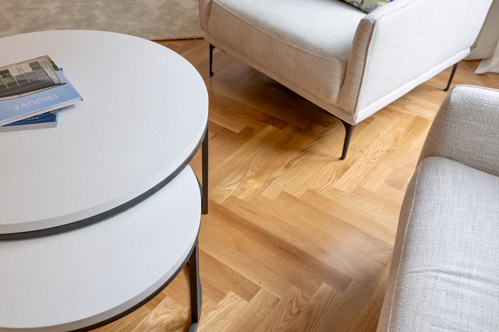 Sala de estar moderna con mesas redondas blancas, sofá beige y piso de madera. Estilo minimalista y elegante con detalles como libros sobre la mesa.