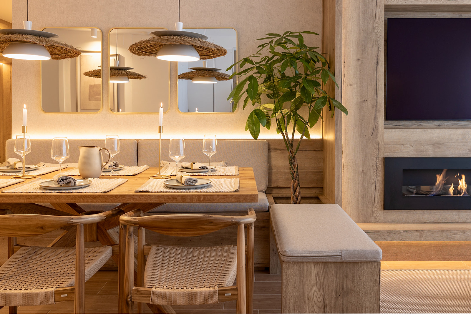 Comedor acogedor con estilo mediterráneo, mesa de madera, lámparas de paja, espejos en la pared, planta decorativa y chimenea. Ambiente cálido y elegante con tonos naturales.