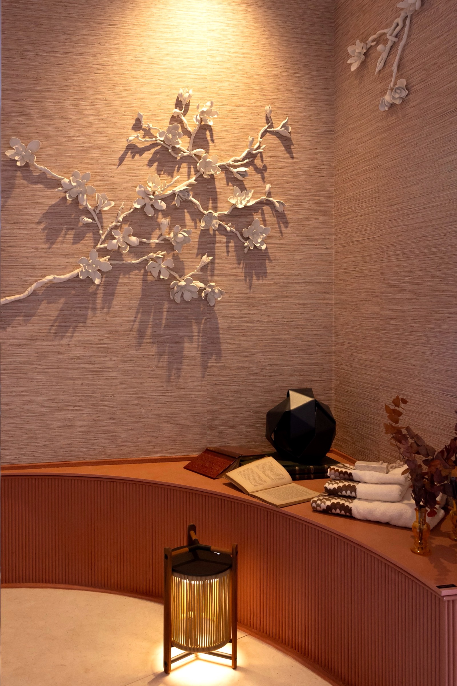 Rama decorativa blanca en pared texturizada con lámpara de pie dorada y estante curvo con libros y objetos decorativos