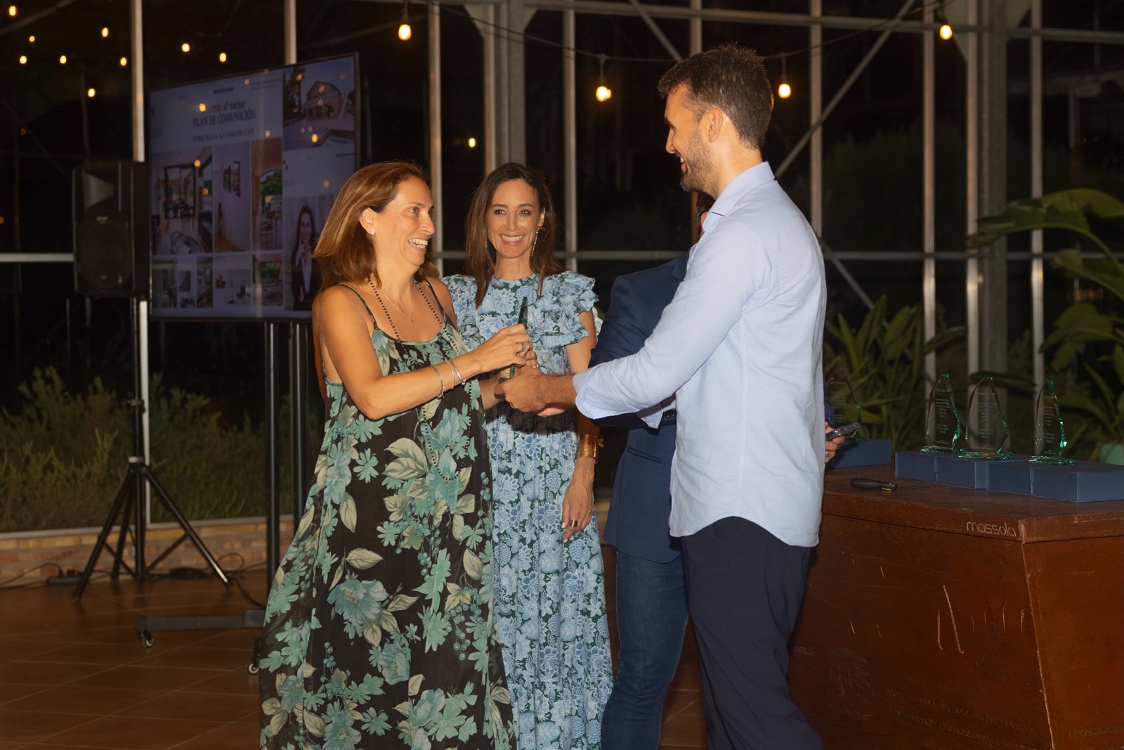 Tres personas vestidas elegantemente en un evento corporativo conversando, con luces cálidas e iluminación de fondo