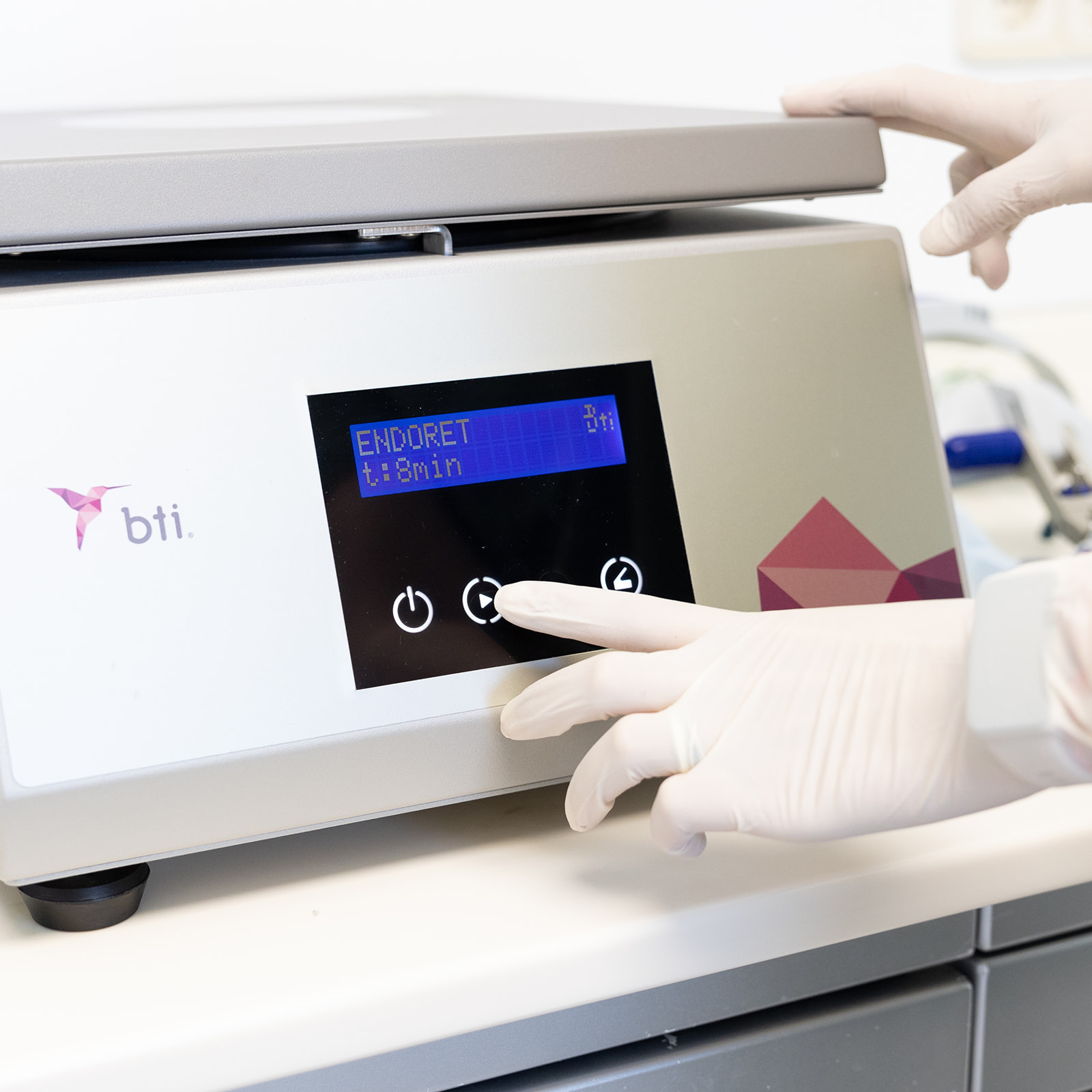 Imagen de una centrífuga de laboratorio marca BTI con pantalla digital mostrando 'ENDORET 1:13min'. Una mano con guante blanco ajusta los controles del equipo.