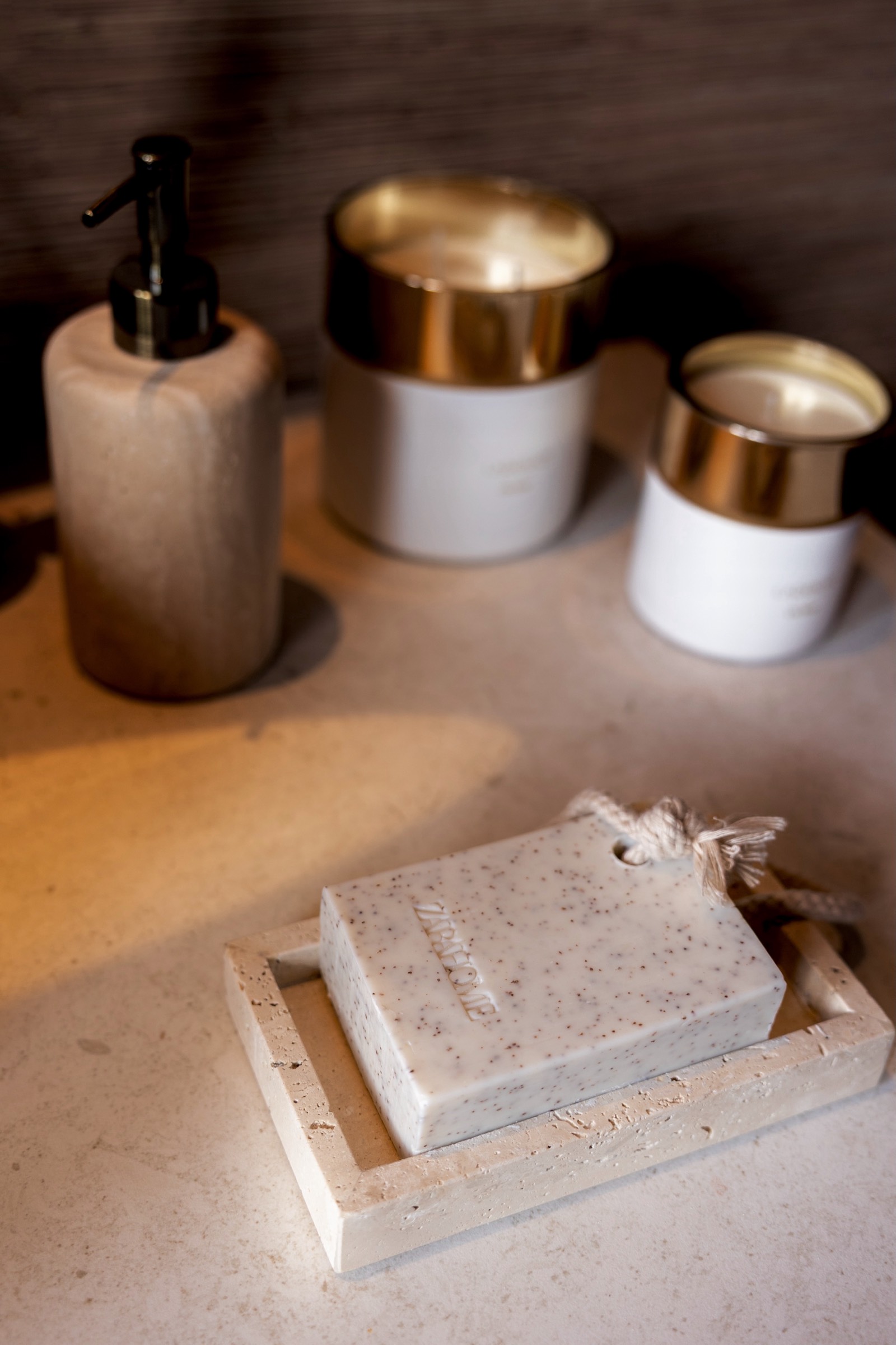 Jabón artesanal con textura de piedra sobre base de piedra, junto a dispensador y frascos dorados y blancos en un entorno minimalista