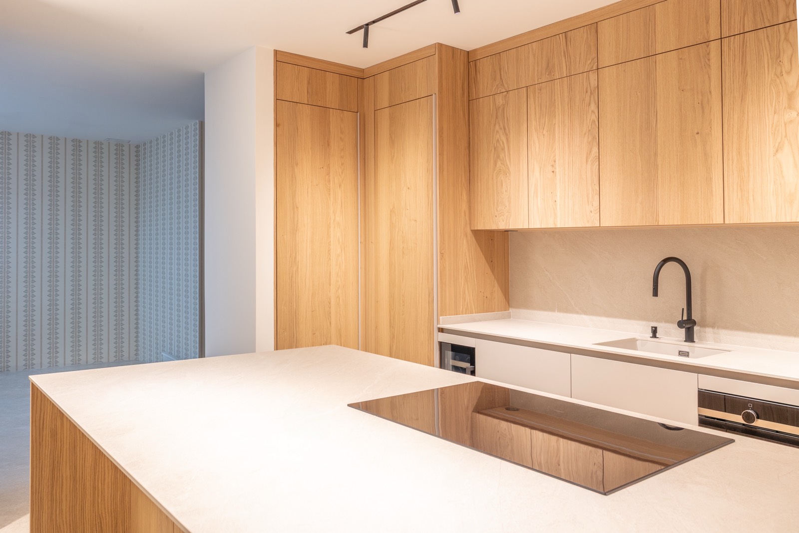 Cocina contemporánea con armarios de madera clara, encimera blanca, fregadero negro y electrodomésticos empotrados