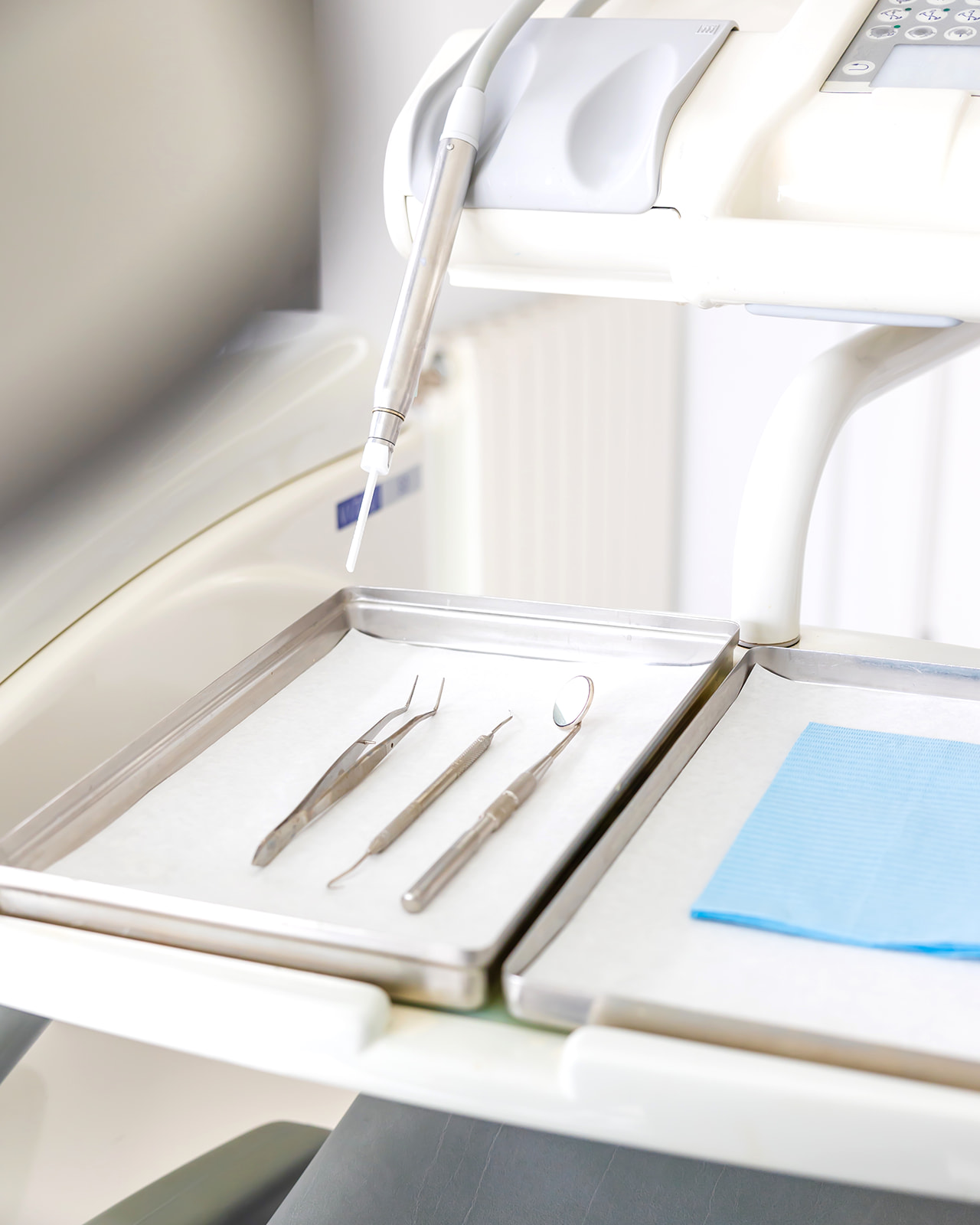 Equipo dental con instrumentos en una bandeja metálica, incluyendo un taladro dental y herramientas de exploración. Se observa una sección del sillón dental y un panel de control en el fondo.