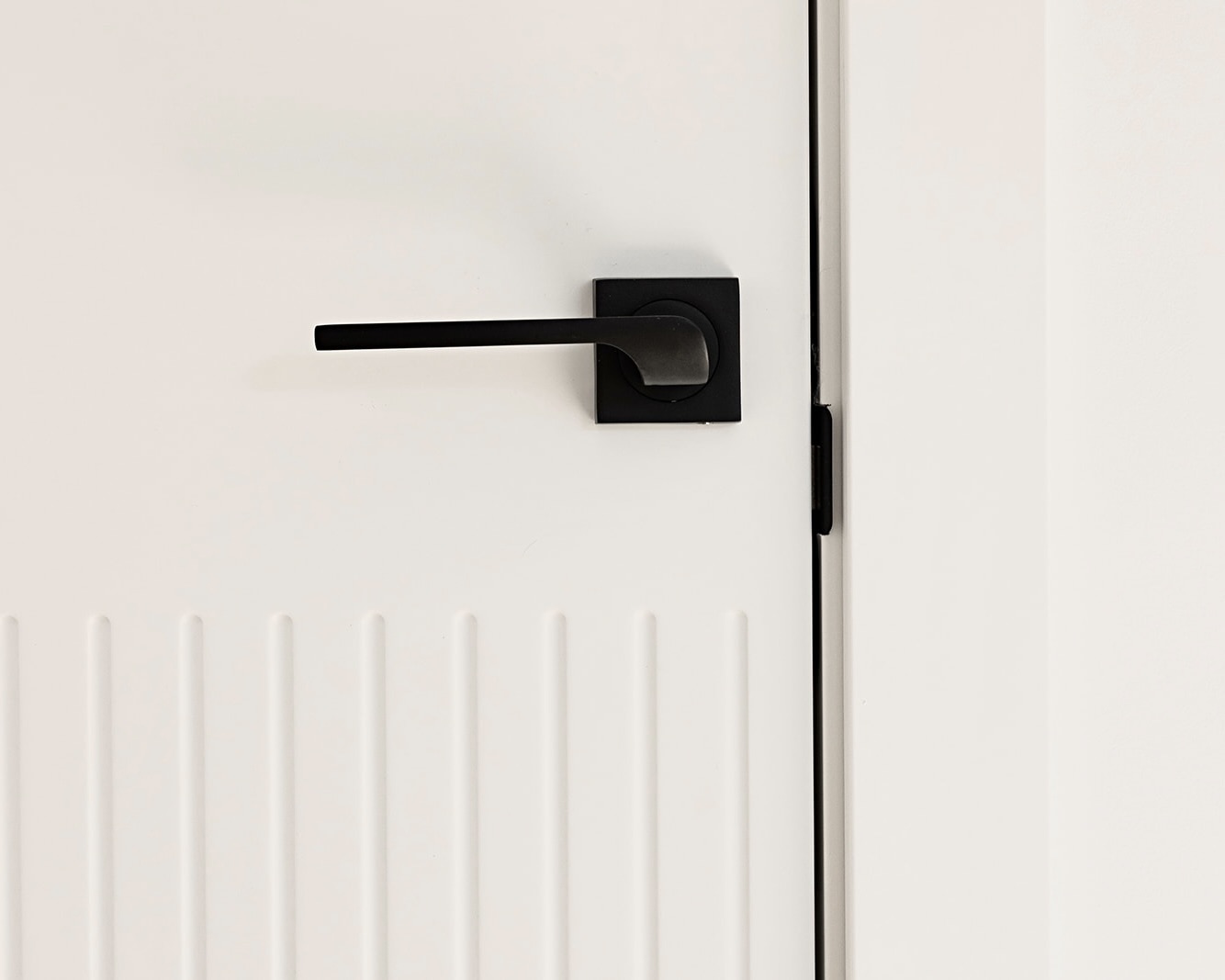 Manija de puerta negra moderna y minimalista en una puerta blanca con paneles decorativos. La manija tiene un diseño rectangular con una palanca horizontal delgada.