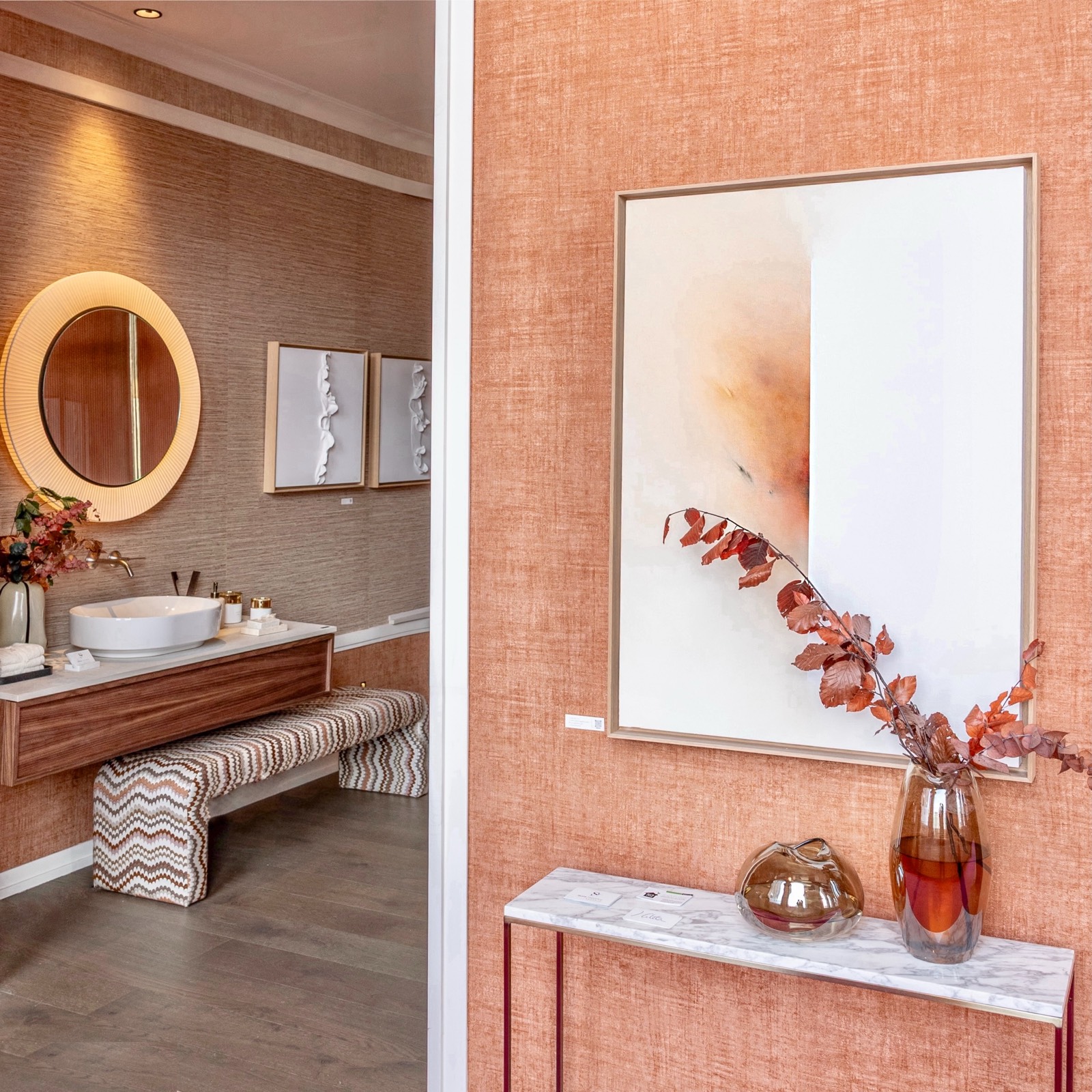 Diseño interior de baño contemporáneo con lavabo blanco, espejo redondo iluminado y decoración en tonos terracota y madera