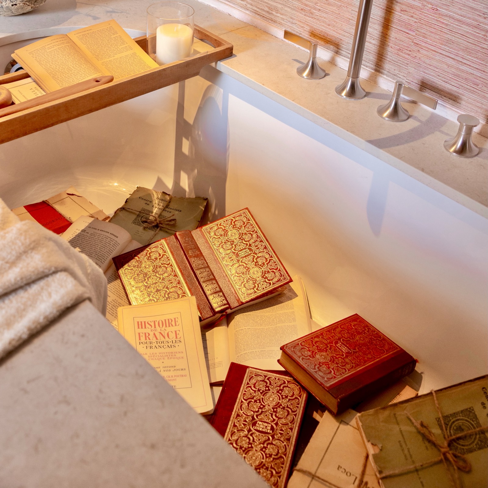 Libros antiguos de historia francesa con cubiertas rojas y doradas, junto a una vela encendida en un ambiente luminoso y tranquilo