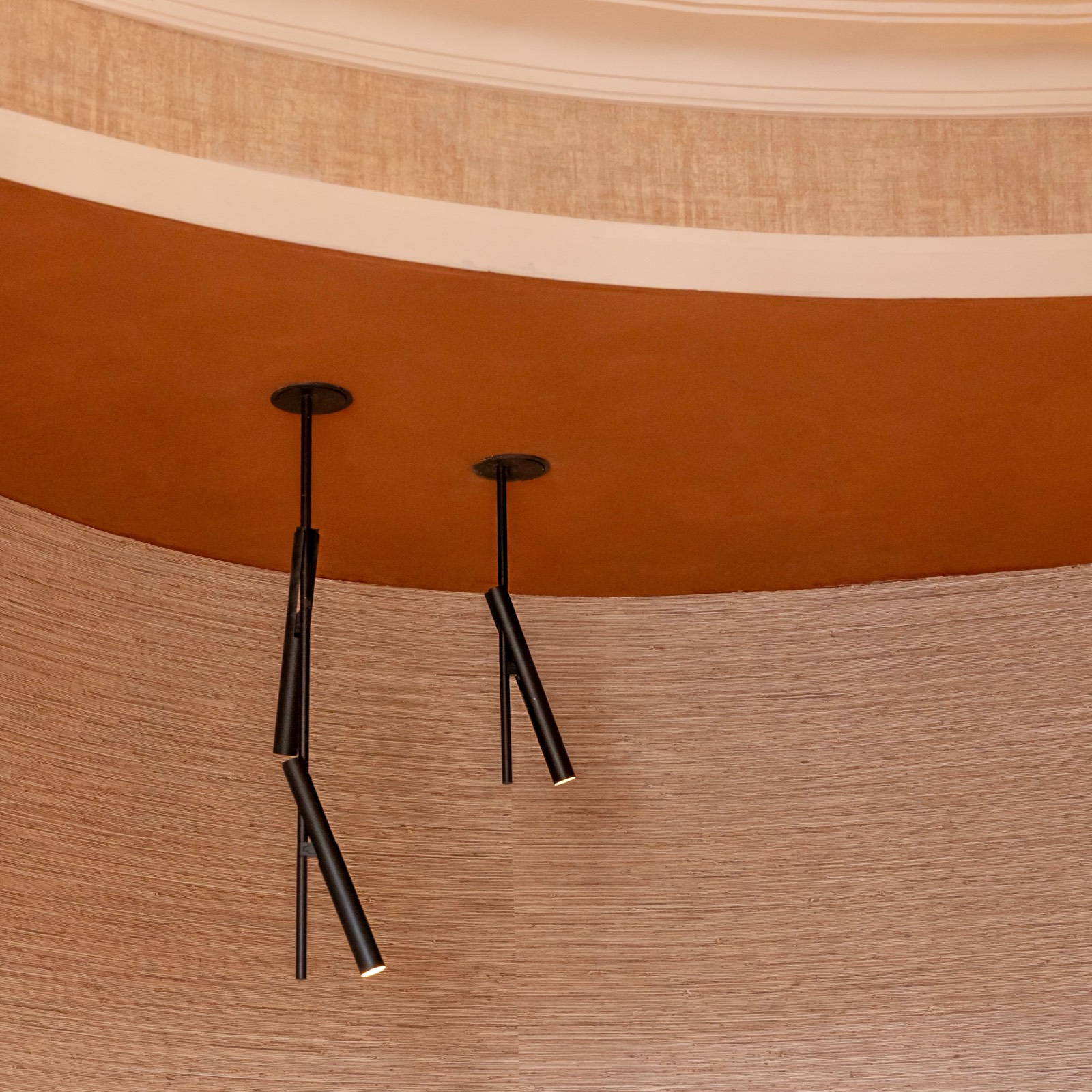 Tres lámparas colgantes delgadas y negras suspendidas en un techo curvo con tonos naranjas y marrones de textura de madera