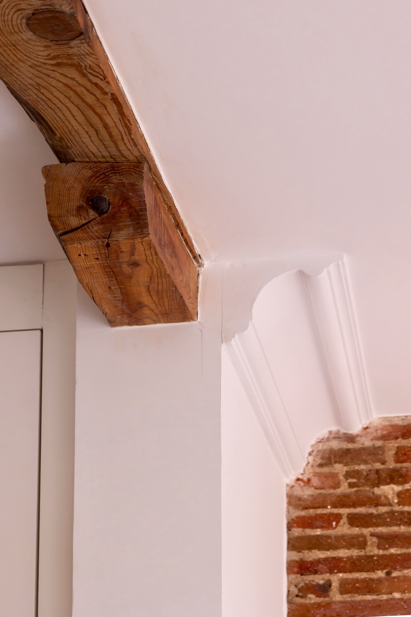 Detalle arquitectónico con viga de madera rústica en esquina de pared blanca, revelando textura de ladrillo expuesto