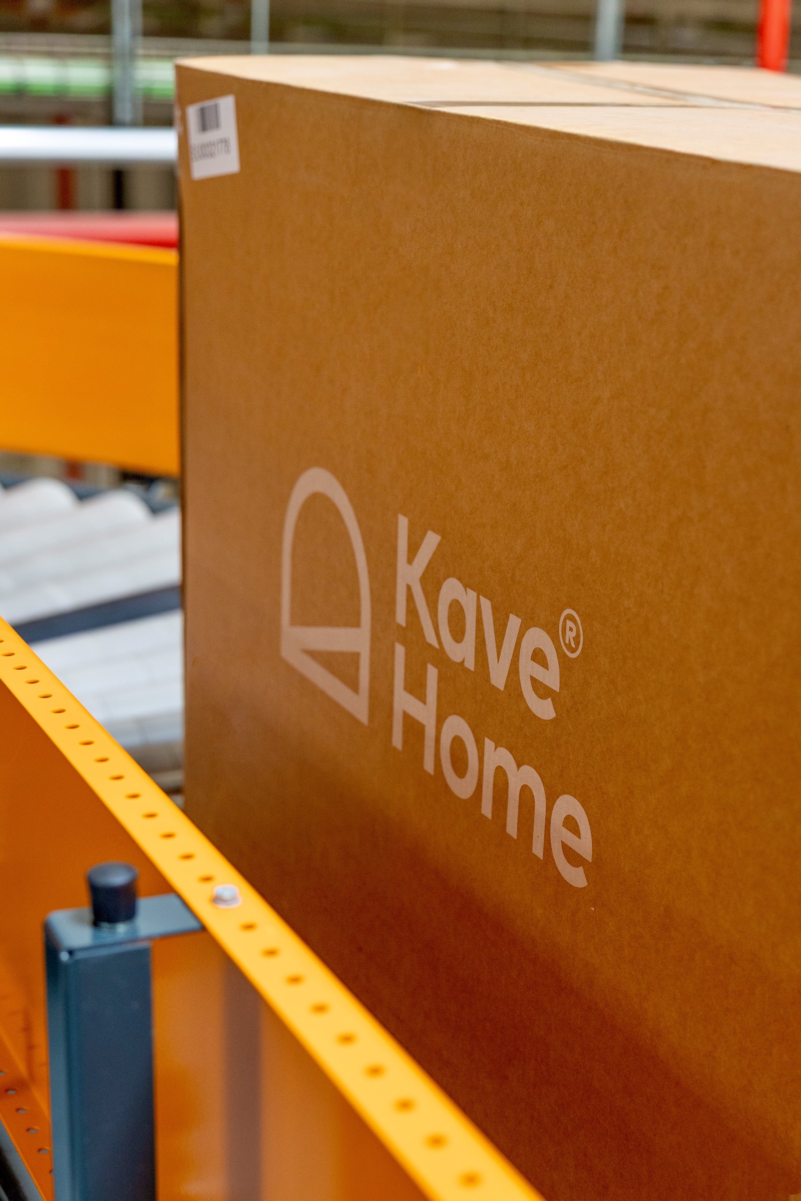 Caja de cartón marrón de la marca Kave Home en un estante de almacén con estanterías amarillas
