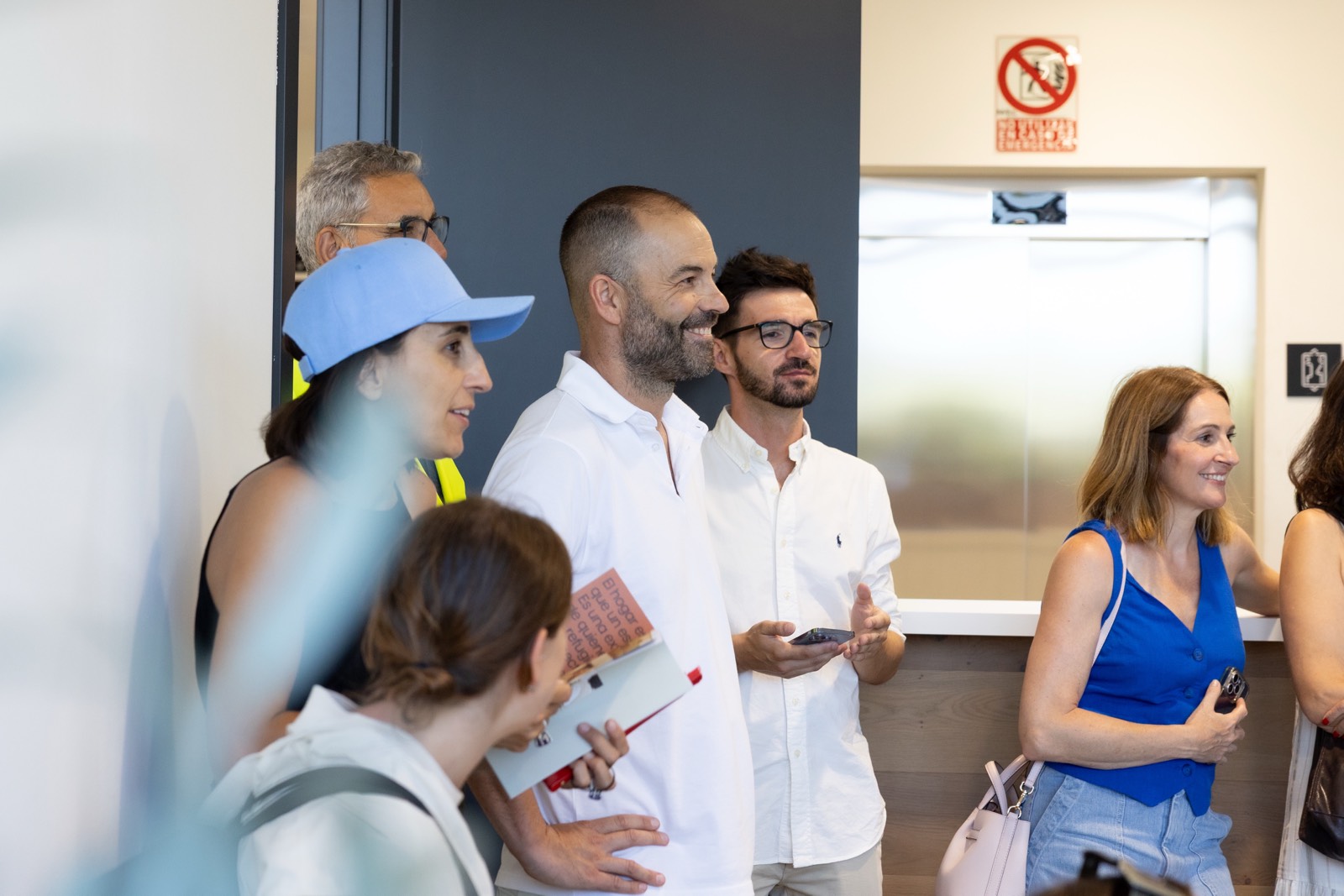 Grupo de personas en una oficina moderna, vestidos de manera casual, algunos con documentos, sonriendo y conversando