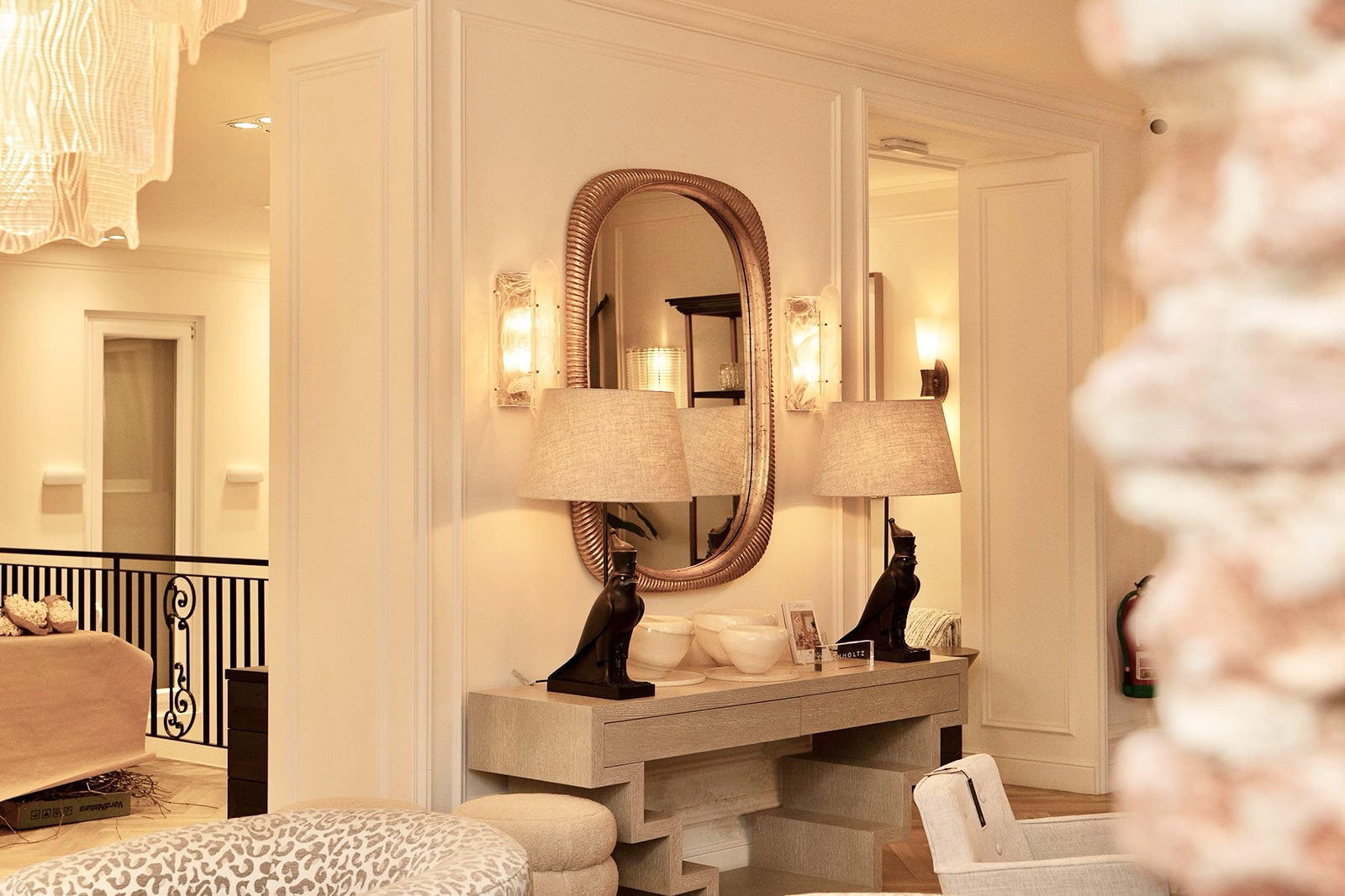 Interior elegante de un hall de entrada con espejo ovalado, lámparas de pared, consola con figuras de gatos egipcios, y una decoración en tonos cálidos y beige