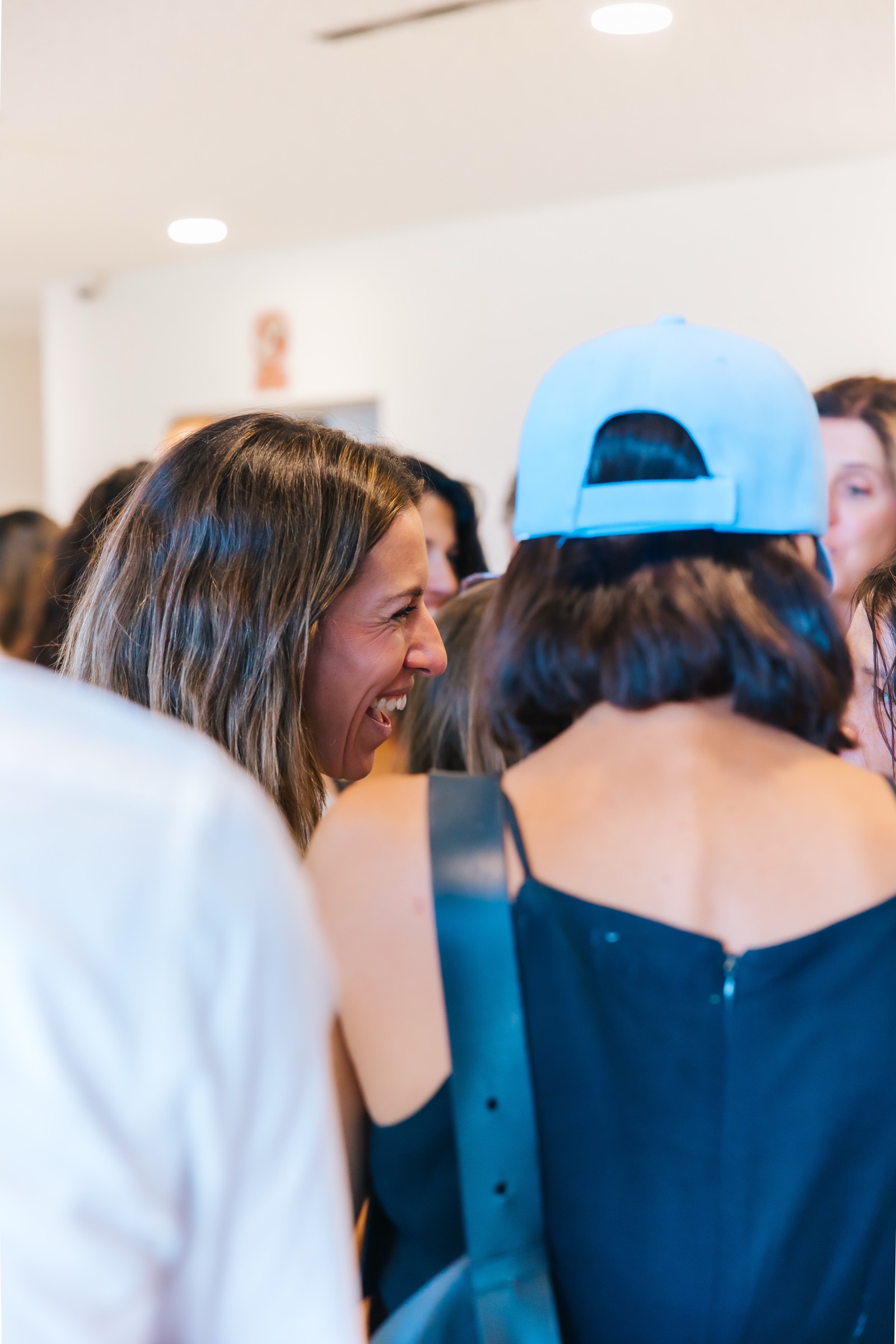 Grupo de personas reunidas, con una persona sonriendo ampliamente y otra de espaldas usando una gorra azul