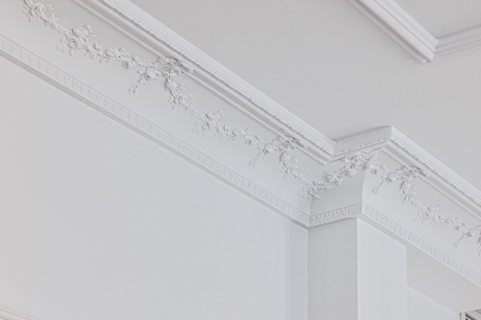 Detalle de una elegante moldura de techo blanca con decoraciones florales en relieve, mostrando un diseño clásico y refinado en la intersección entre la pared y el techo