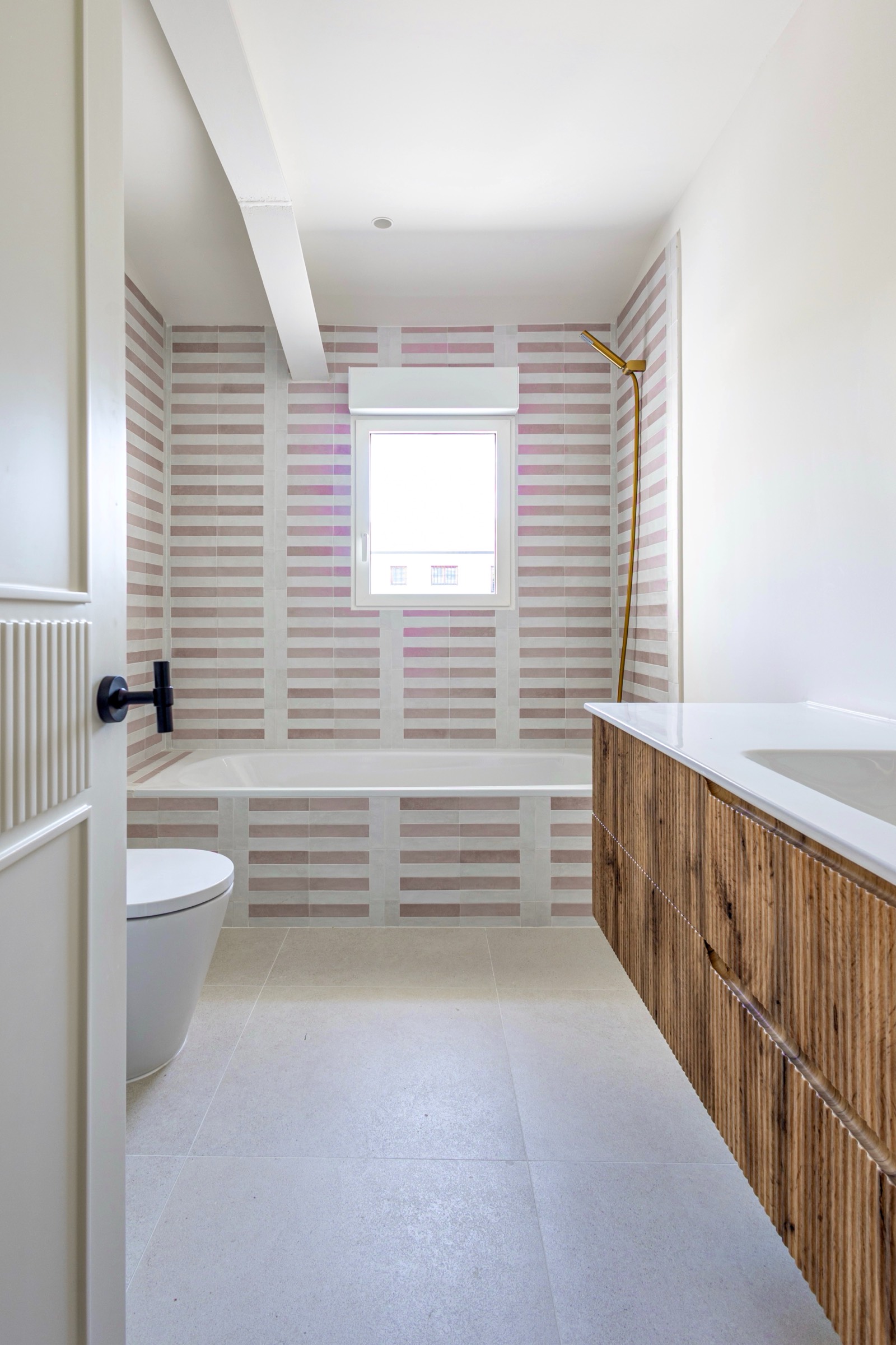 Baño contemporáneo con paredes de azulejos rayados en tonos neutros, mueble de madera y sanitarios blancos