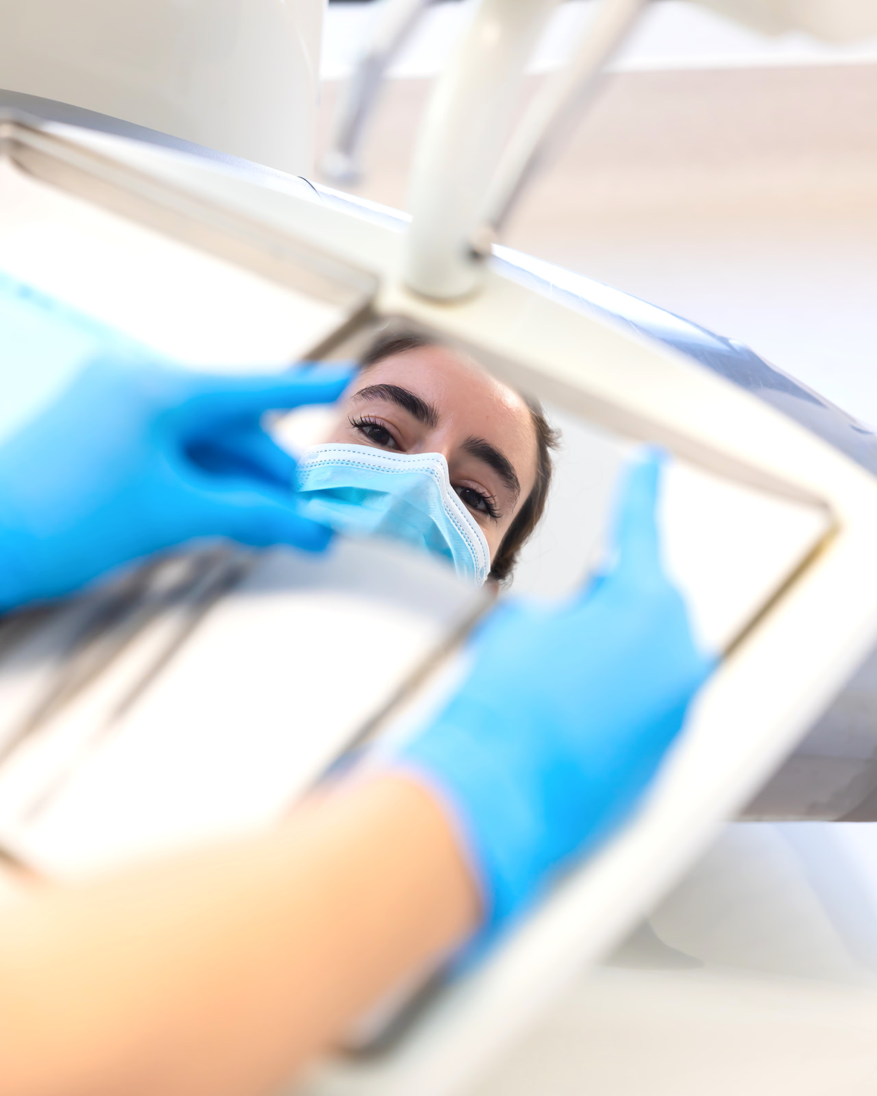 Vista desde la perspectiva de un paciente dental. Se ve a un profesional de la salud dental con máscara facial y guantes azules trabajando con instrumentos dentales sobre el paciente.