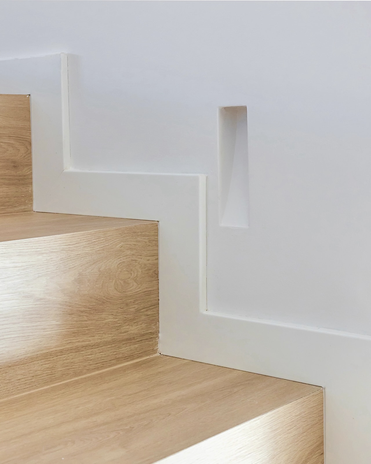 Escalera minimalista con peldaños de madera clara y paredes blancas. Los escalones tienen un acabado natural que contrasta con el blanco limpio de las paredes, creando un diseño elegante y moderno.