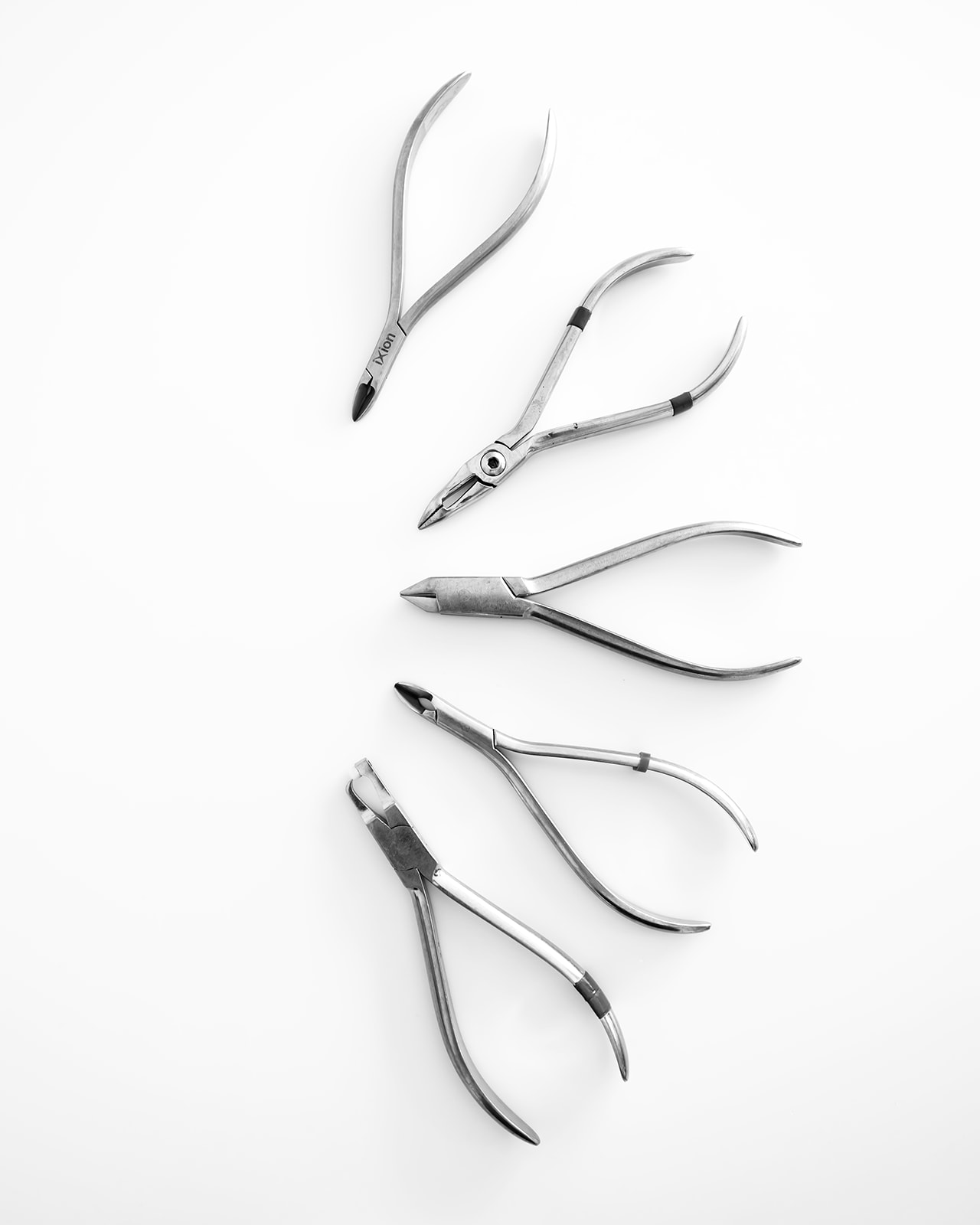 Conjunto de cinco herramientas de manicura y pedicura de acero inoxidable sobre fondo blanco. Incluye alicates, cortaúñas y pinzas de diferentes formas y tamaños para el cuidado de uñas y cutículas.
