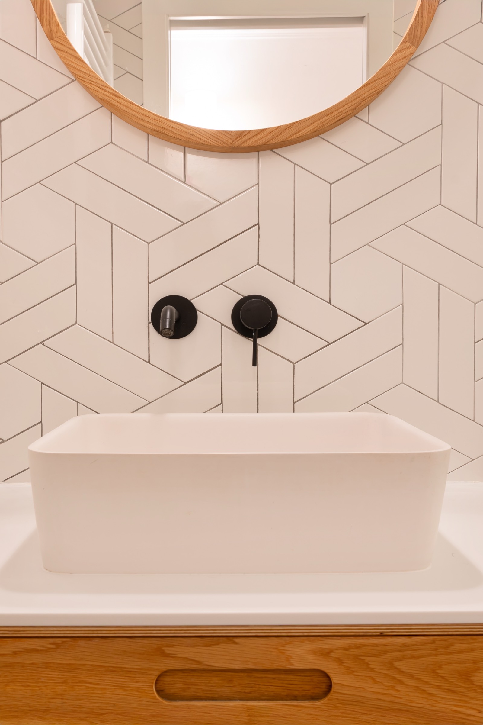 Lavabo rectangular blanco con grifería negra empotrada, instalado sobre pared de azulejos geométricos blancos y mueble de madera