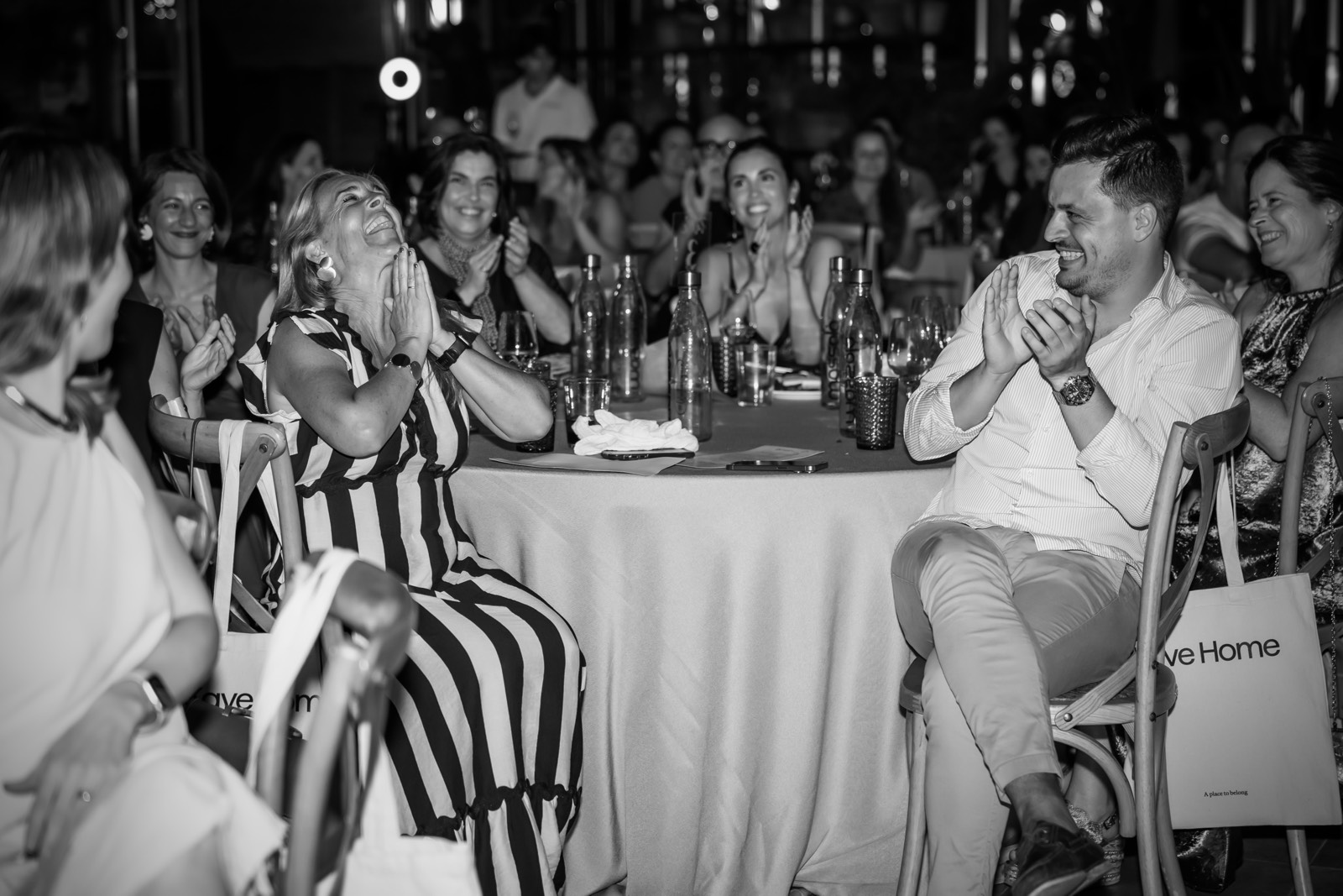 Grupo de personas sentadas alrededor de una mesa, riendo y aplaudiendo en un evento social nocturno