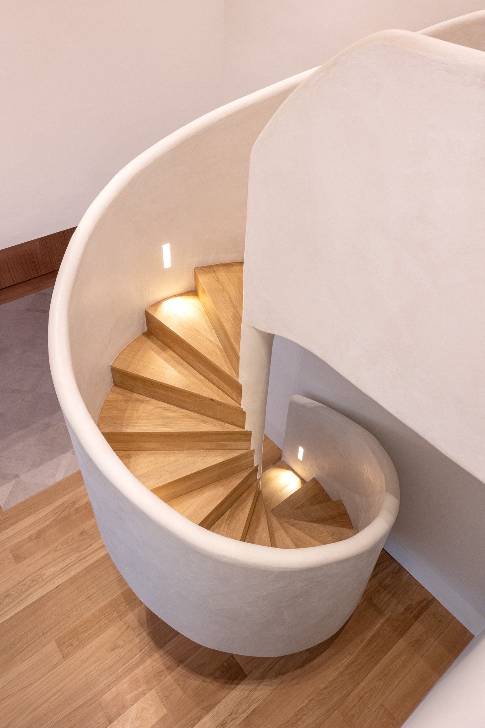 Escalera de caracol moderna con peldaños de madera clara y paredes curvas blancas, con iluminación suave integrada