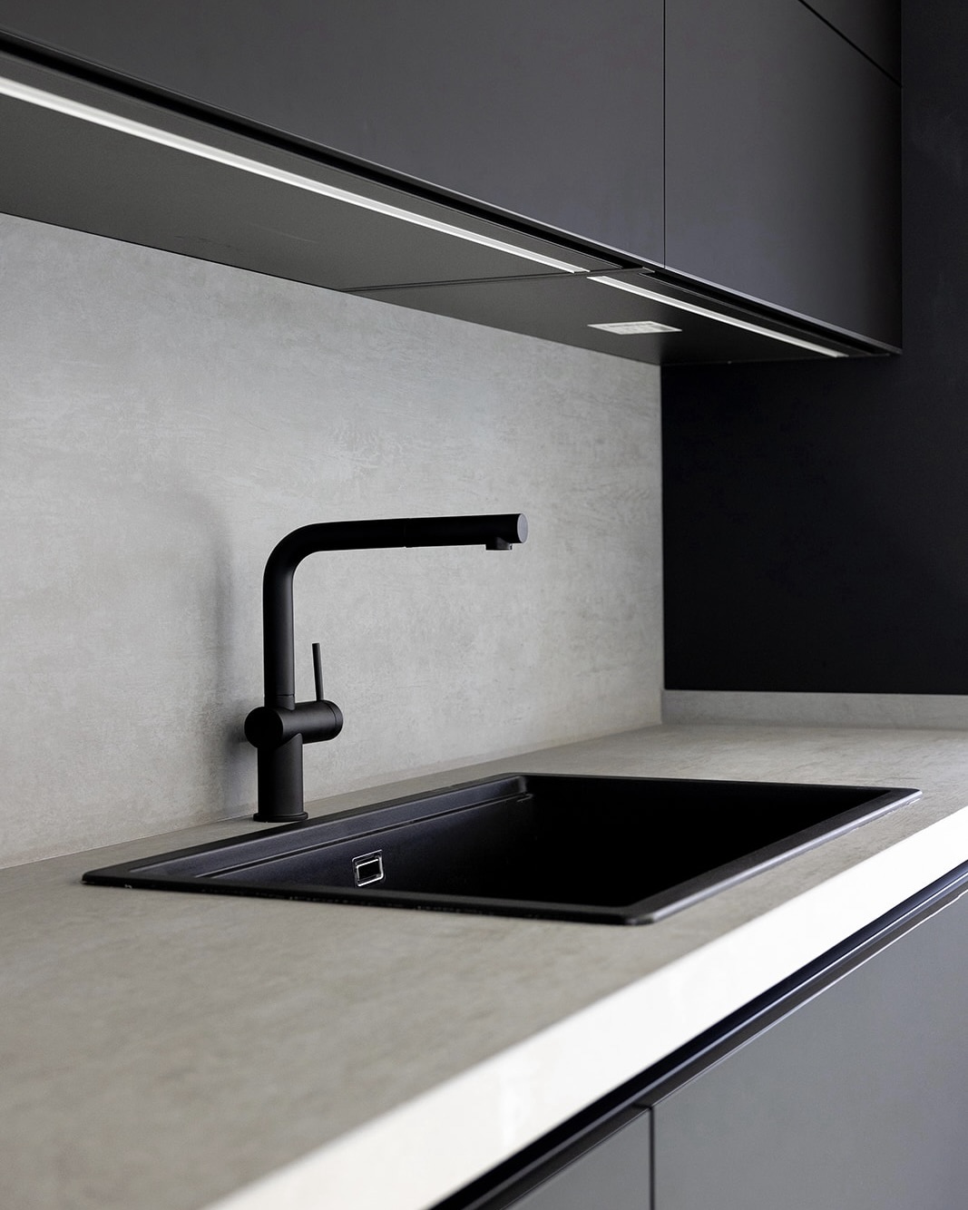Cocina moderna con diseño minimalista en tonos negro y gris. Fregadero negro empotrado con grifo negro de diseño curvo. Encimera gris claro y armarios superiores negros con iluminación LED integrada.