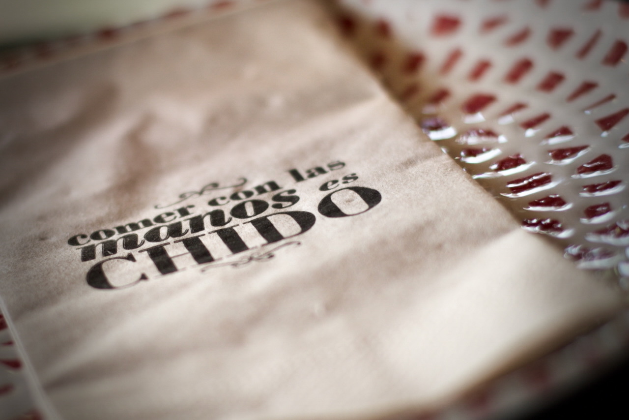 Primer plano de texto impreso en papel vintage que dice 'comer con las manos es chido', con detalles de textura y patrones rojos en el borde del documento