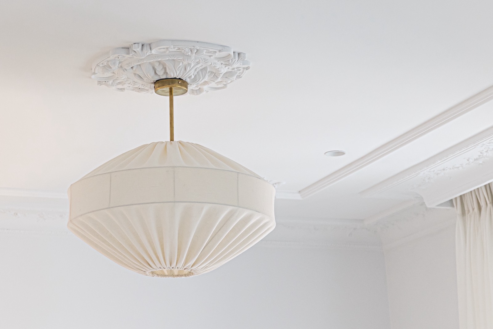 Lámpara de techo colgante blanca con forma de farol, suspendida de un medallón decorativo en un techo blanco con molduras ornamentales