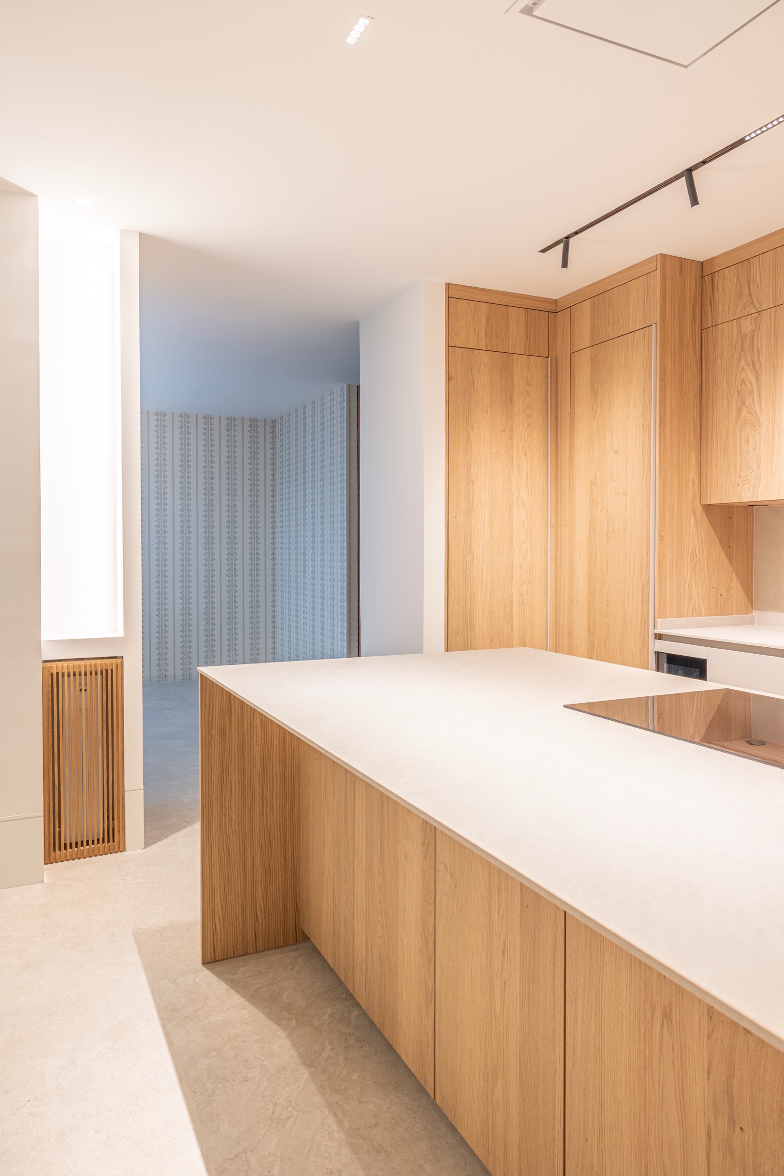 Interior de cocina moderna con diseño minimalista, gabinetes de madera clara y encimera blanca con iluminación natural