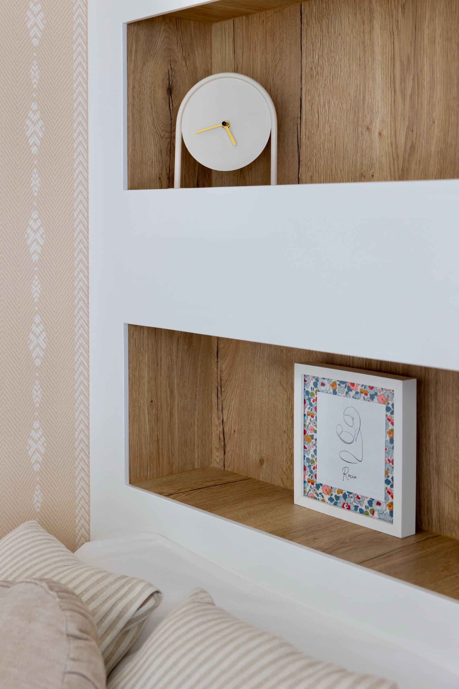 Estantería de madera con un reloj blanco minimalista y un cuadro con marco floral en un espacio decorativo moderno