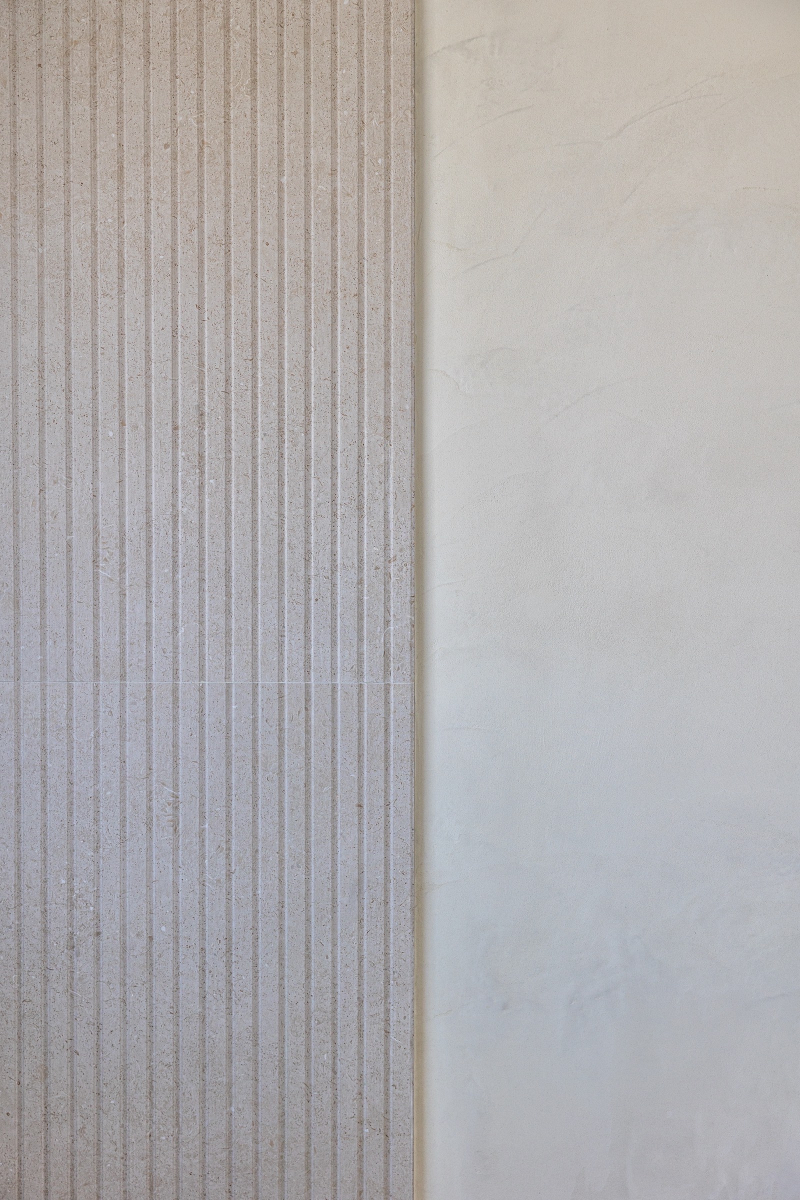 Detalle de pared con superficie acanalada en tonos grises y beige, mostrando líneas verticales y textura rugosa