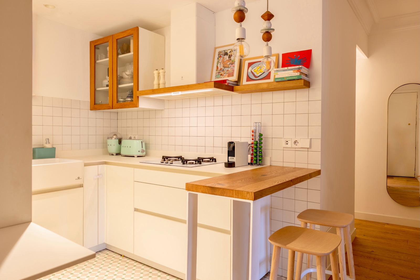 Cocina compacta con diseño minimalista en tonos blancos y madera, con electrodomésticos verdes y estantes decorativos
