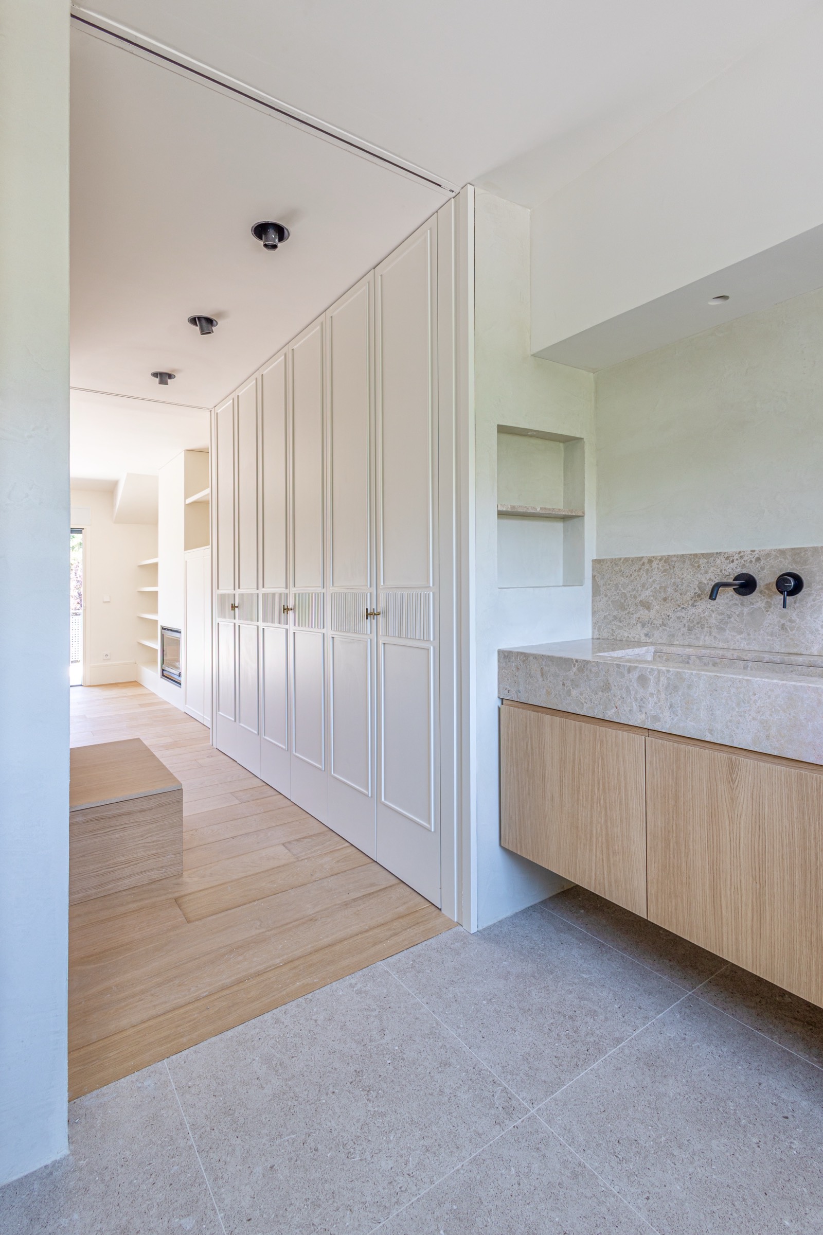 Espacio interior moderno con pared blanca panelada, armarios de madera clara, lavabo de piedra y piso de baldosas grises