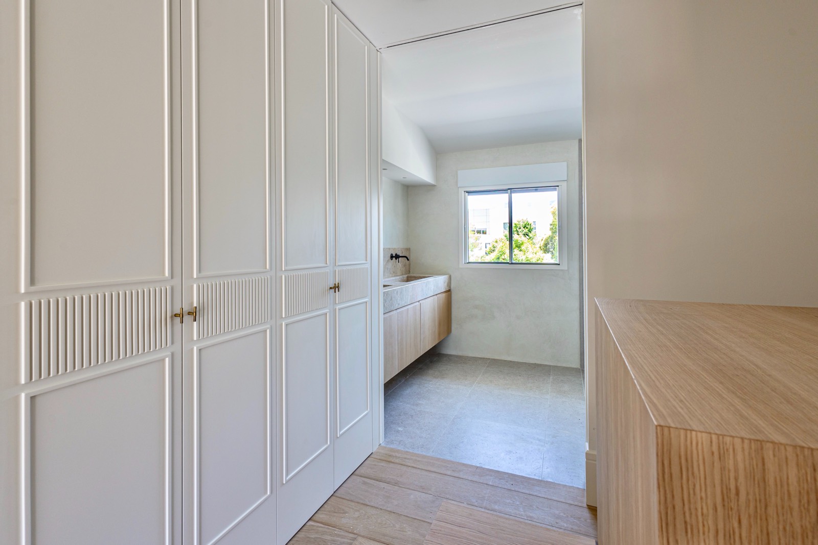 Interior de cocina moderna con armarios blancos de diseño clásico, piso de madera y ventana con luz natural