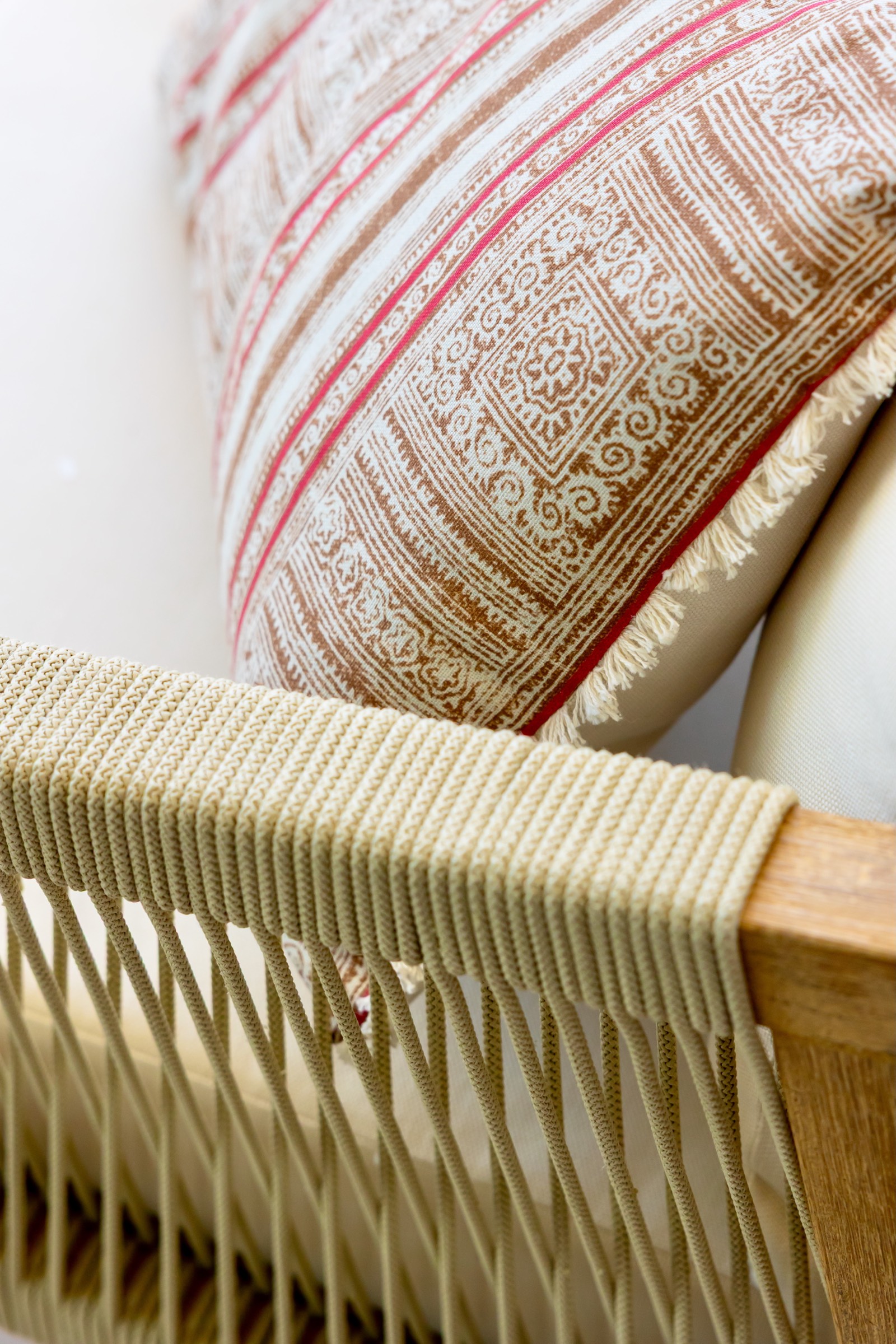 Primer plano de un cojín con patrón geométrico en tonos marrones y rosados sobre un mueble con cuerdas tejidas en el reposabrazos