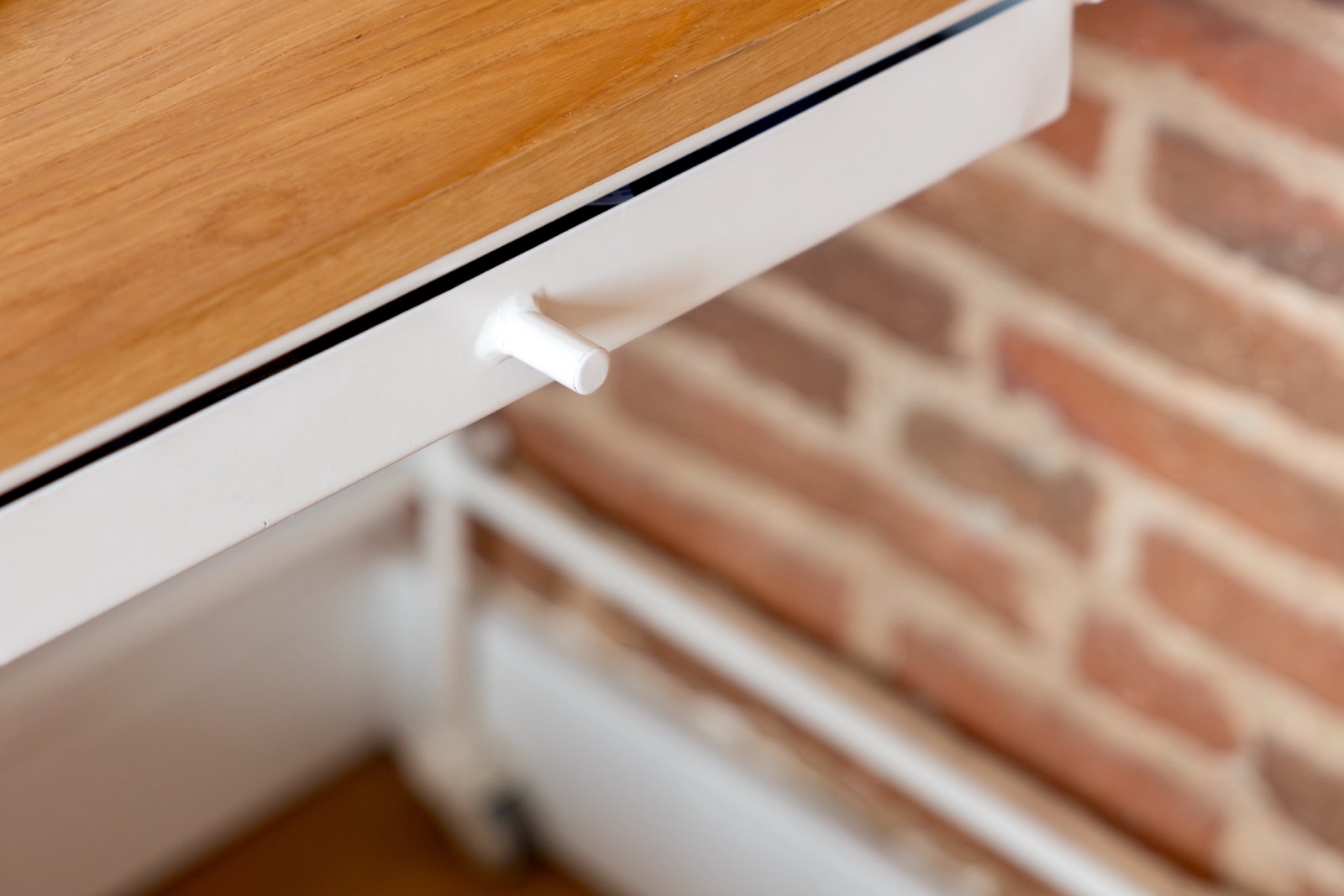 Primer plano de un mueble blanco con tirador pequeño, mostrando textura de madera y pared de ladrillo en el fondo